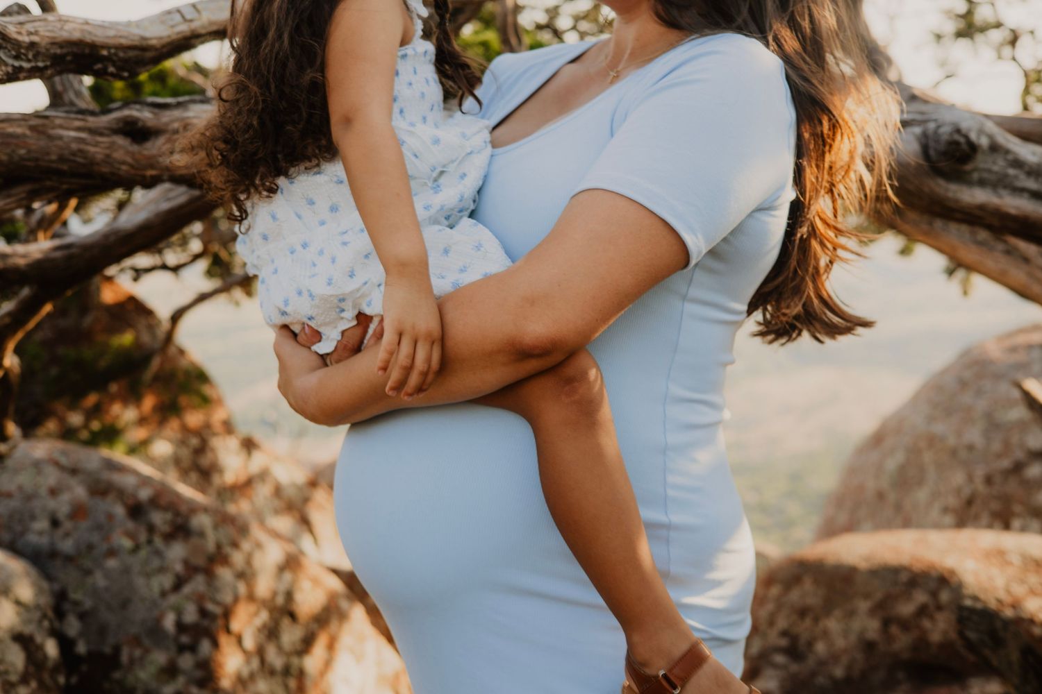Maternity photo showing pregnant belly in white dress against sunlit background.