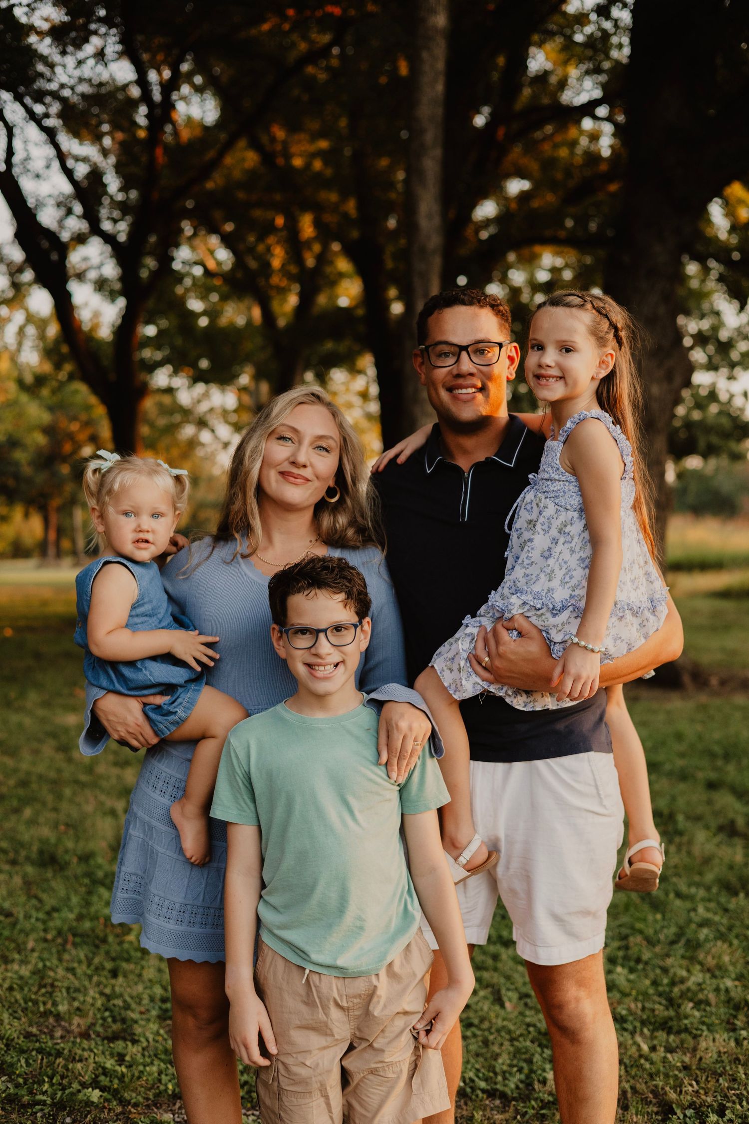 Family of five poses together for a portrait in a park during golden hour.