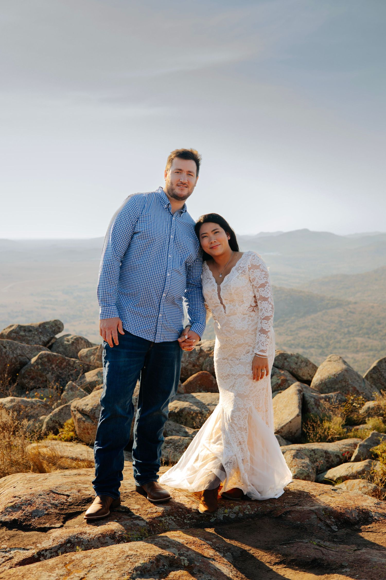 A couple stands together on rocky mountain terrain during their wedding photoshoot.