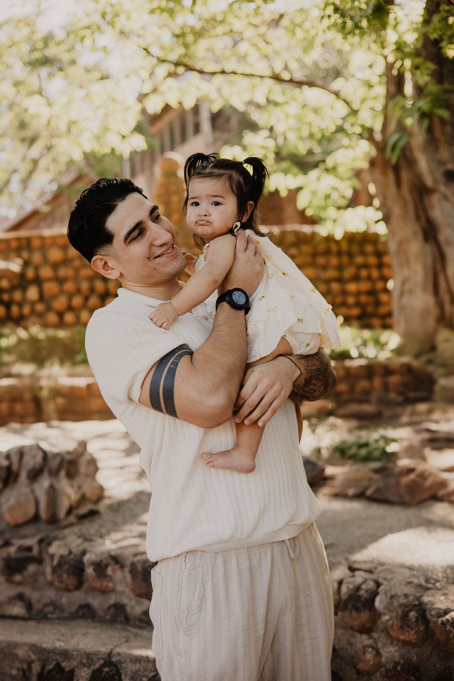 Loving family shares tender moments together in outdoor garden setting with brick wall backdrop.