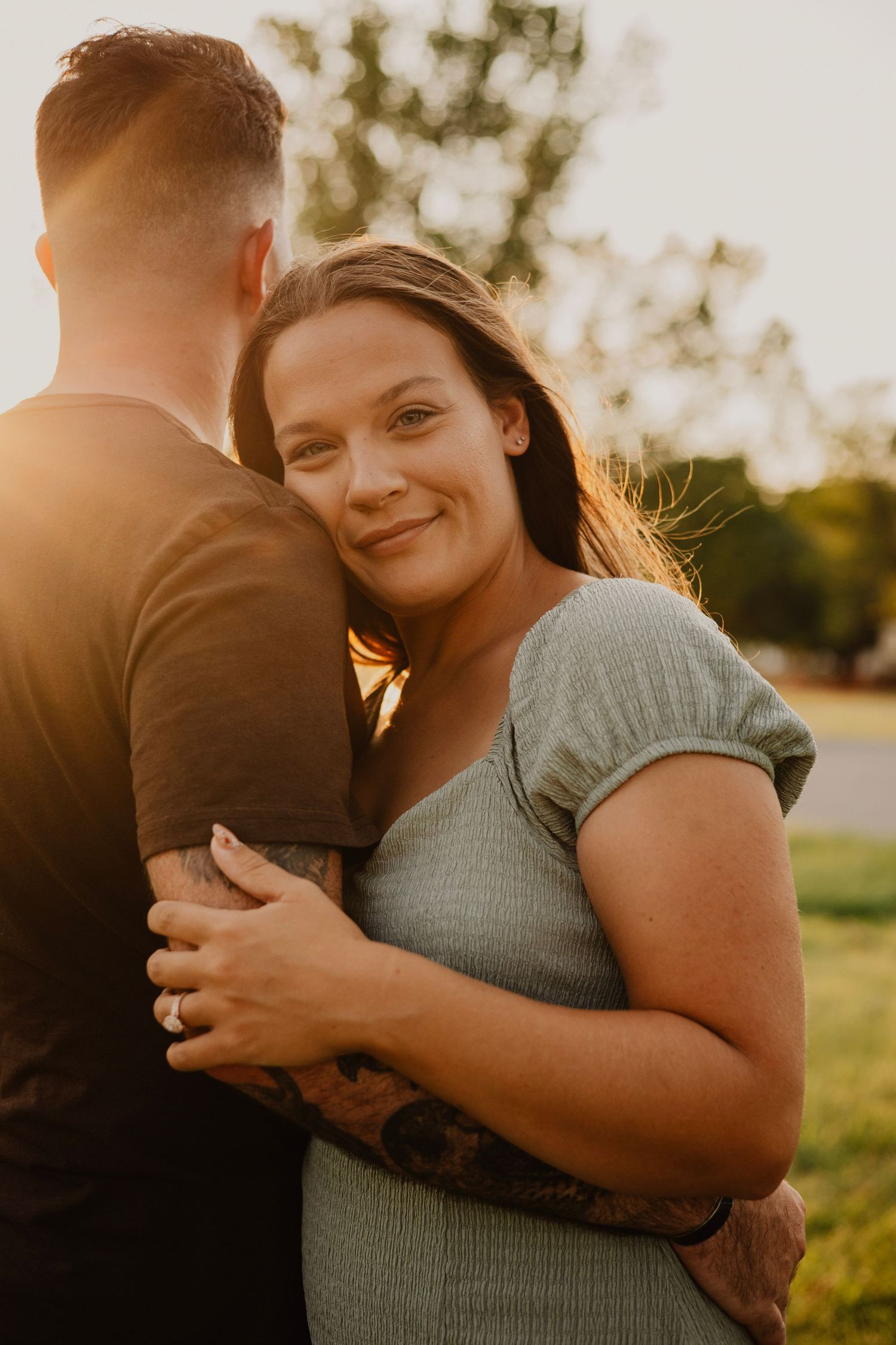 Couple embracing in warm sunset light with woman in sage green dress smiling.