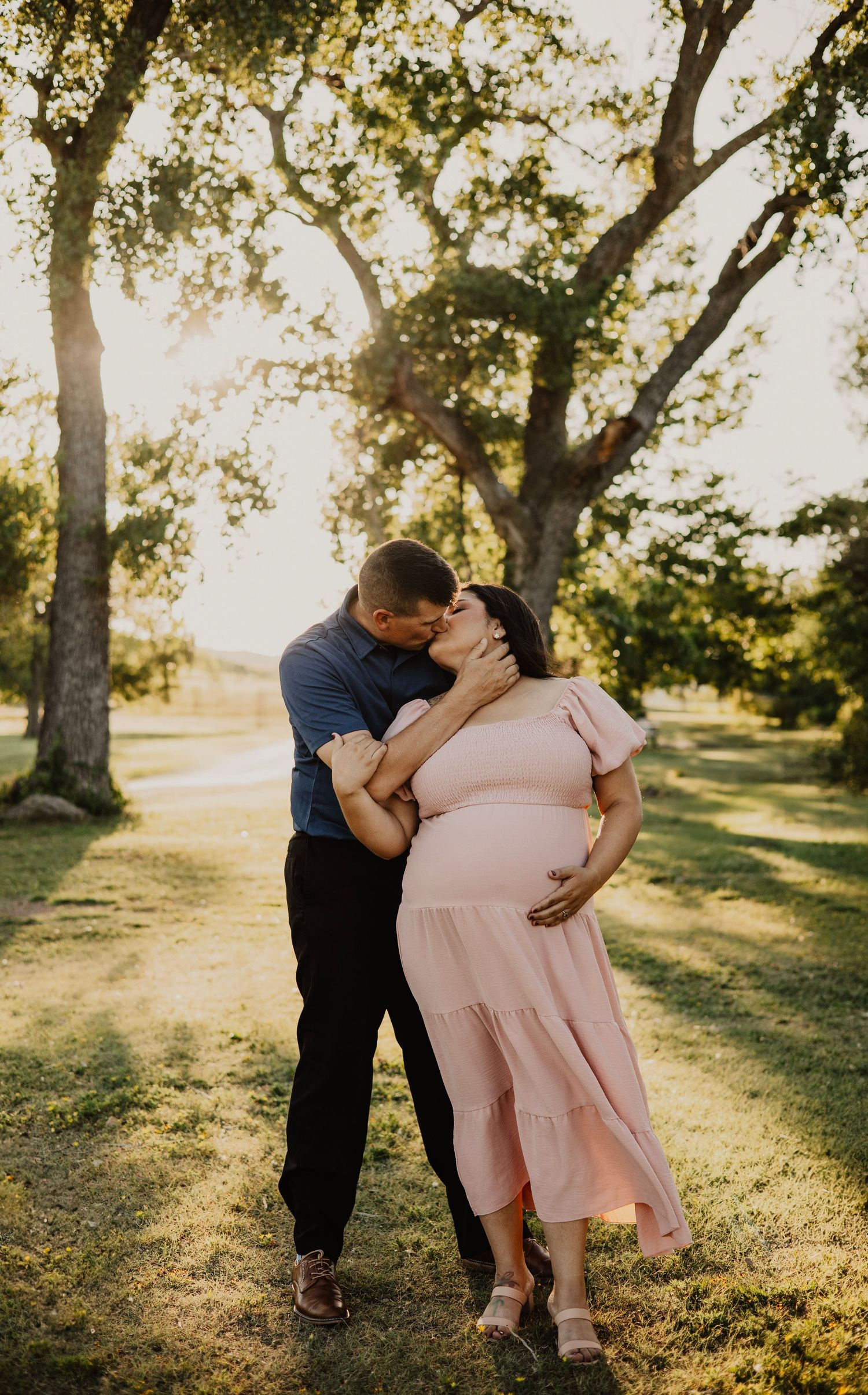 A tender moment between a couple in a park during golden hour with sunlit trees in the background.