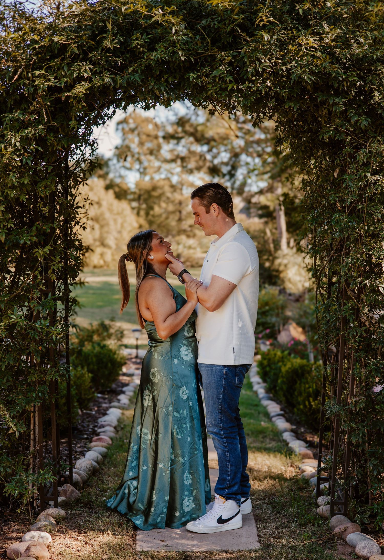 A couple sharing a romantic moment under a garden archway lined with greenery.