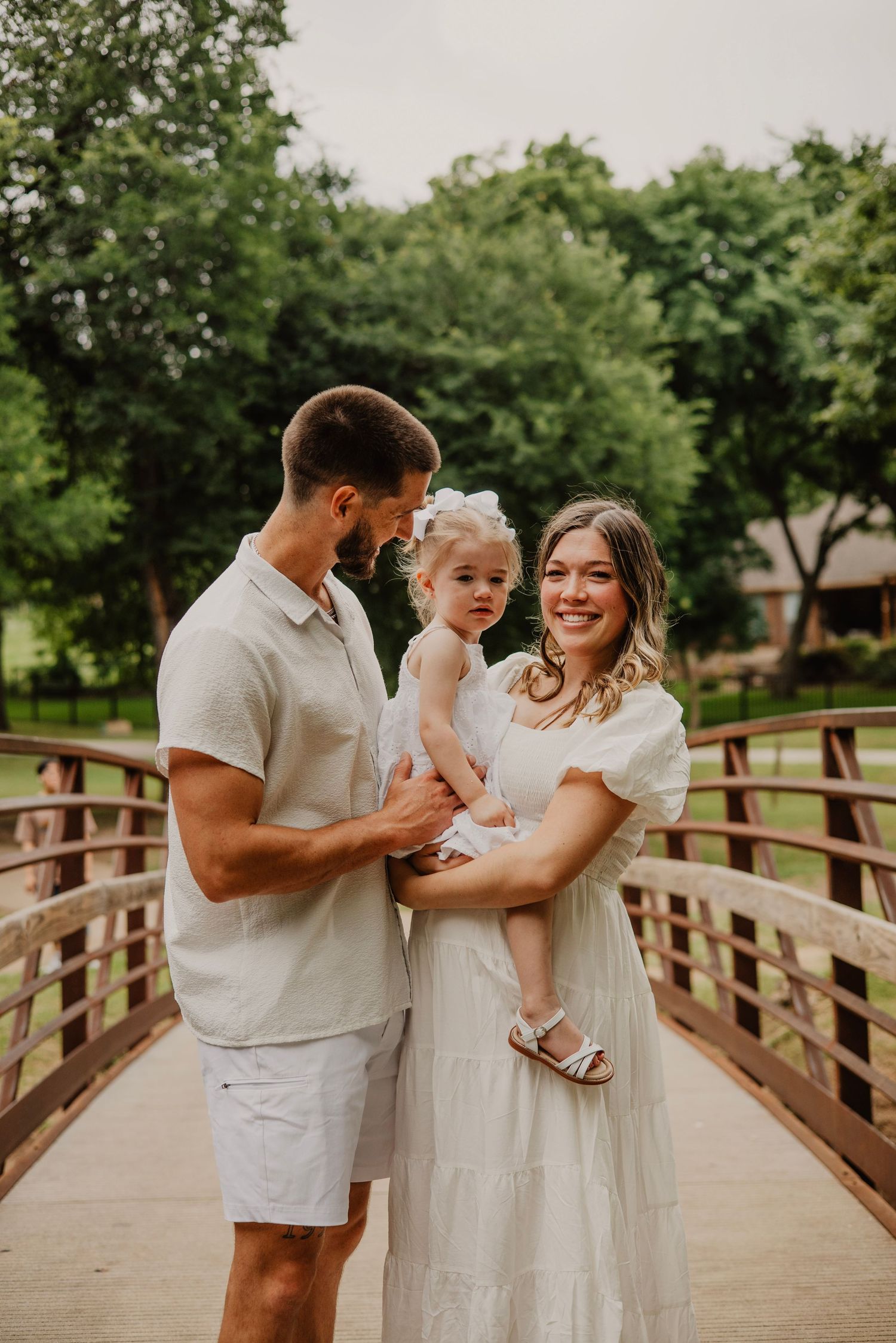 Family shares a joyful moment together while standing on a wooden bridge in a lush park setting.