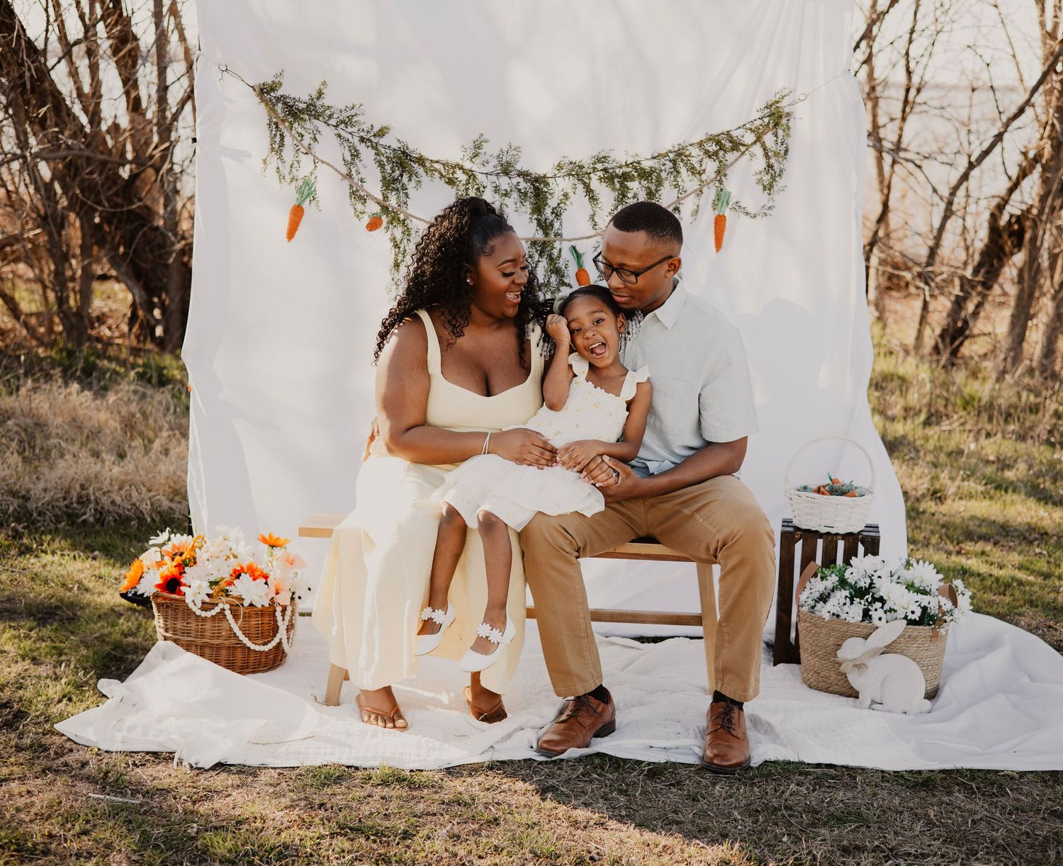 Family photo session outdoors with white backdrop and rustic wooden bench.