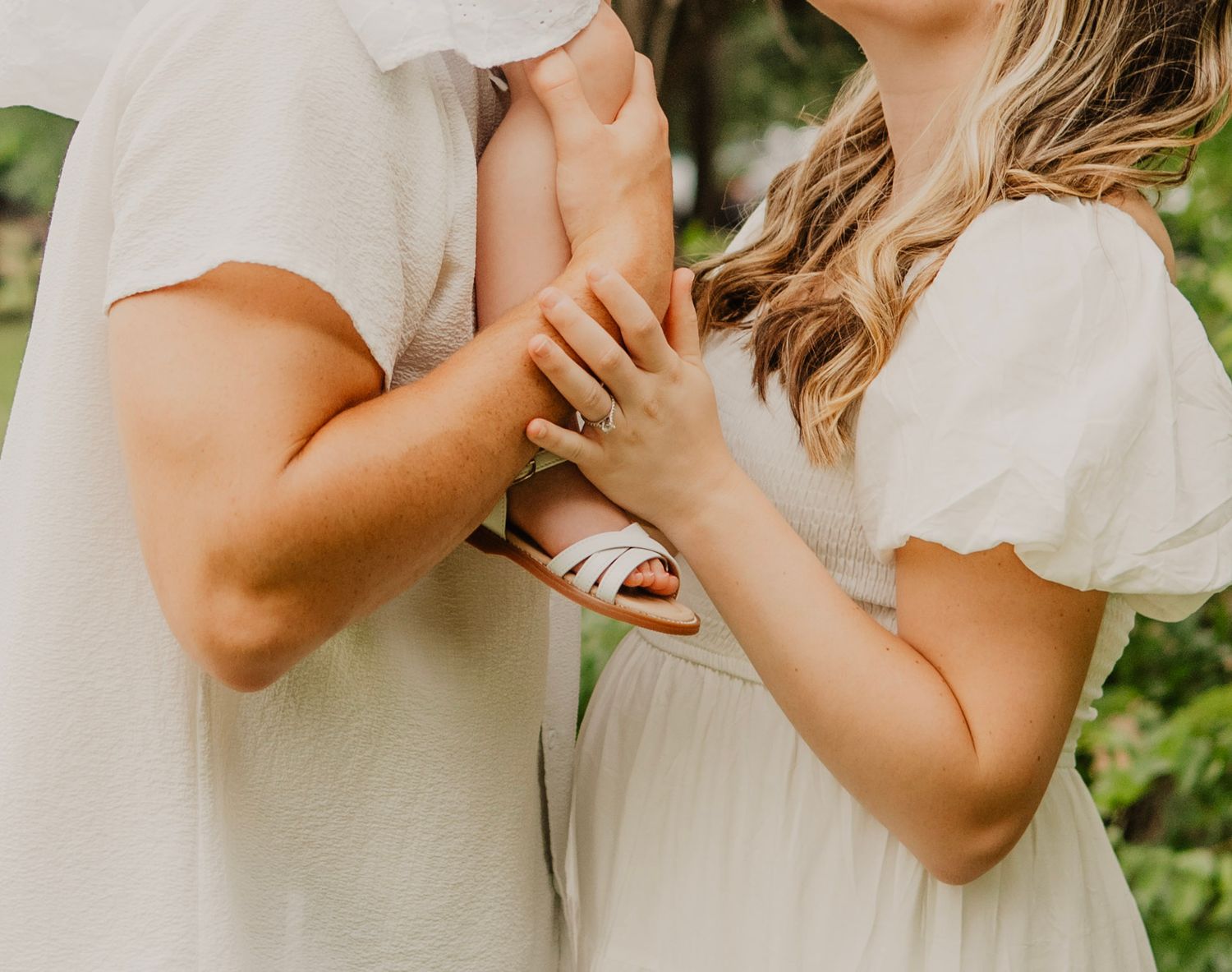 A couple shares an intimate embrace in a lush garden setting wearing white wedding attire.
