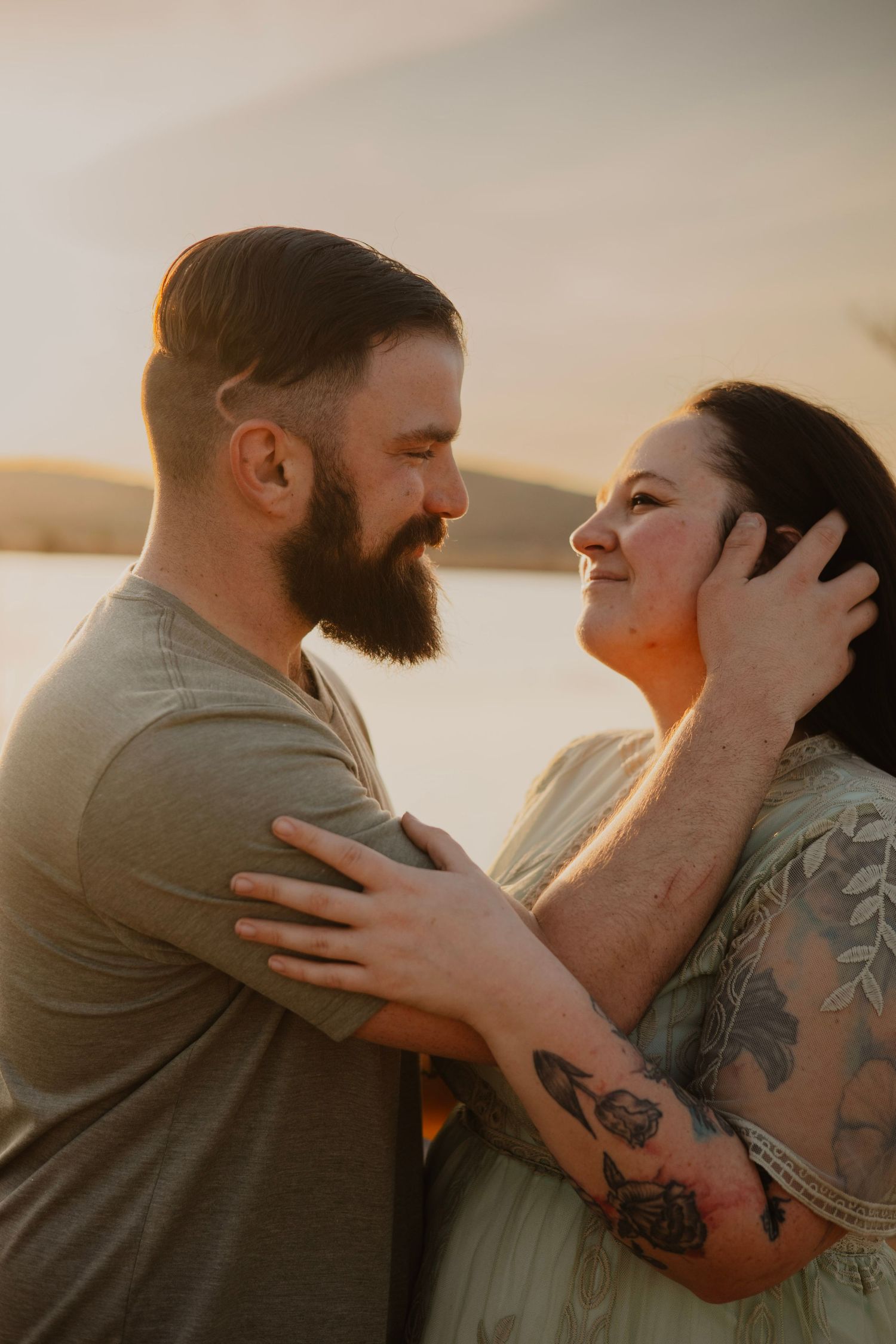 A romantic sunset portrait of a couple embracing with visible tattoos and warm lighting.