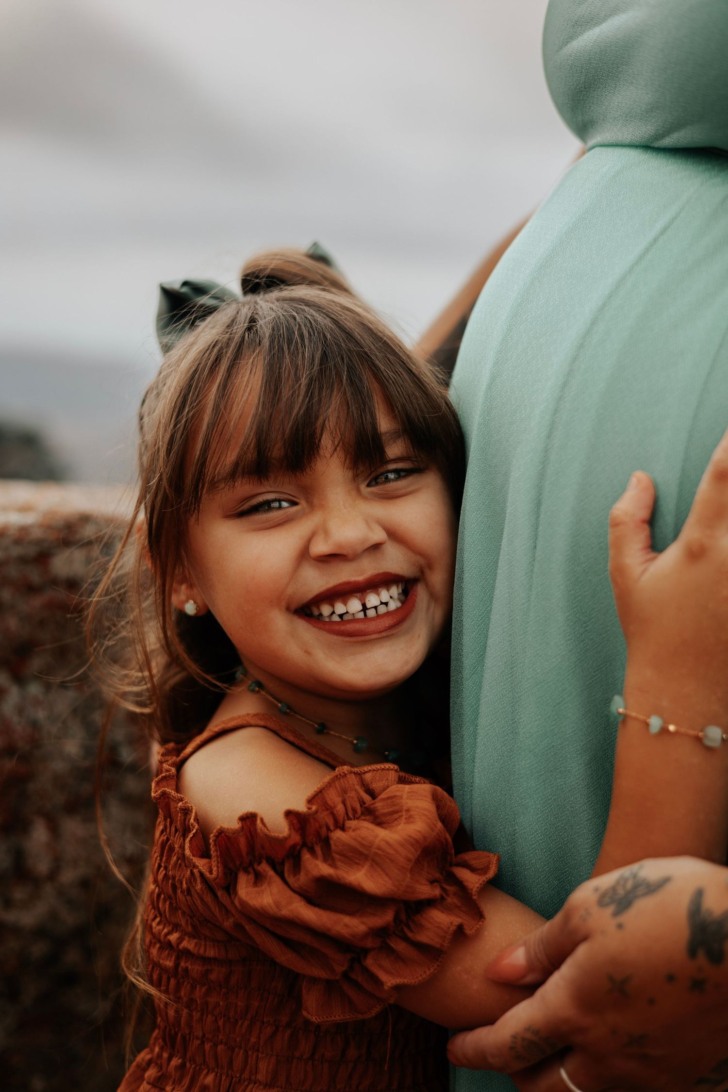 A child in rust-colored dress hugs a pregnant belly while smiling joyfully.