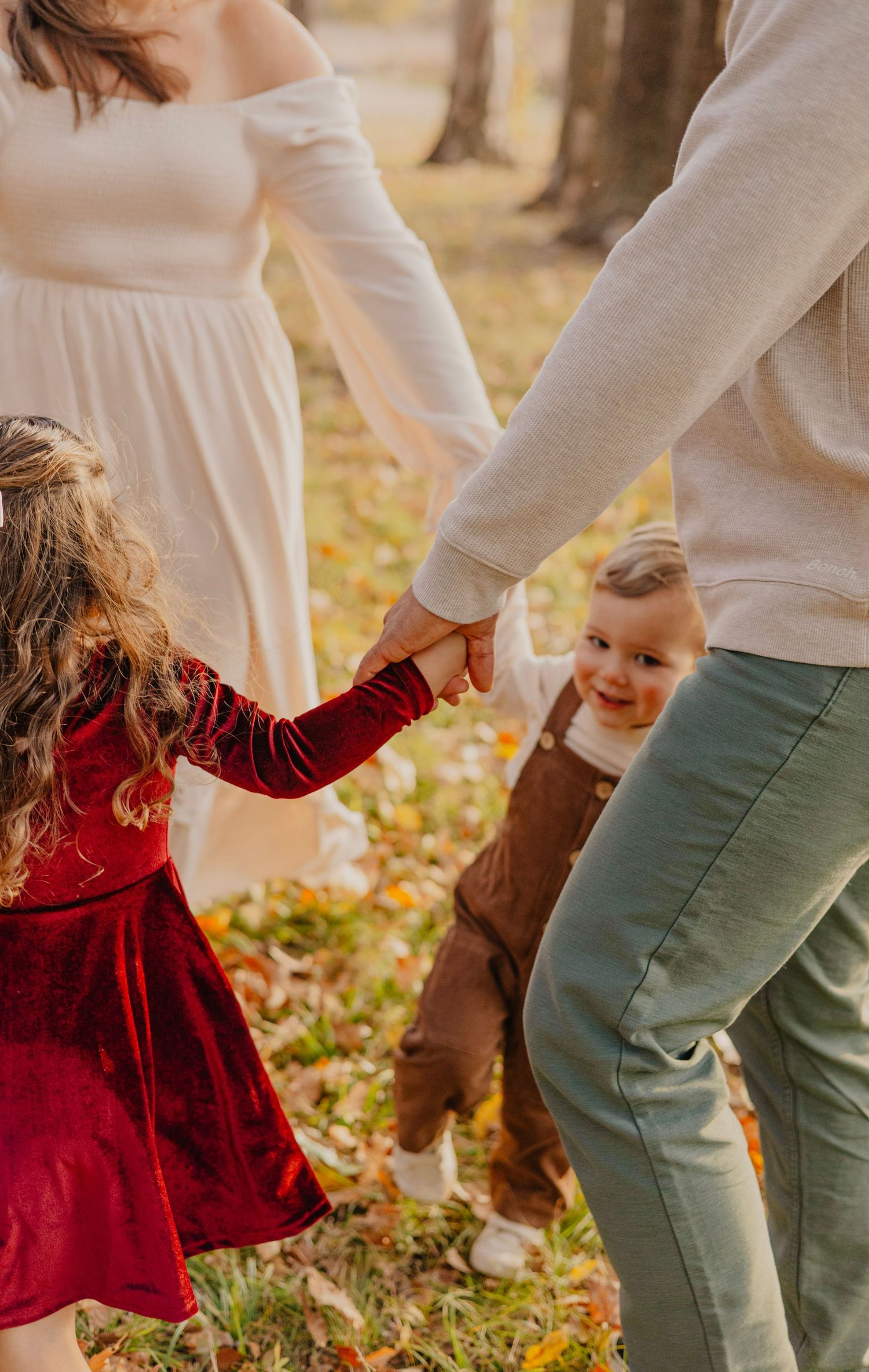 Family holding hands while walking through autumn leaves in a park.