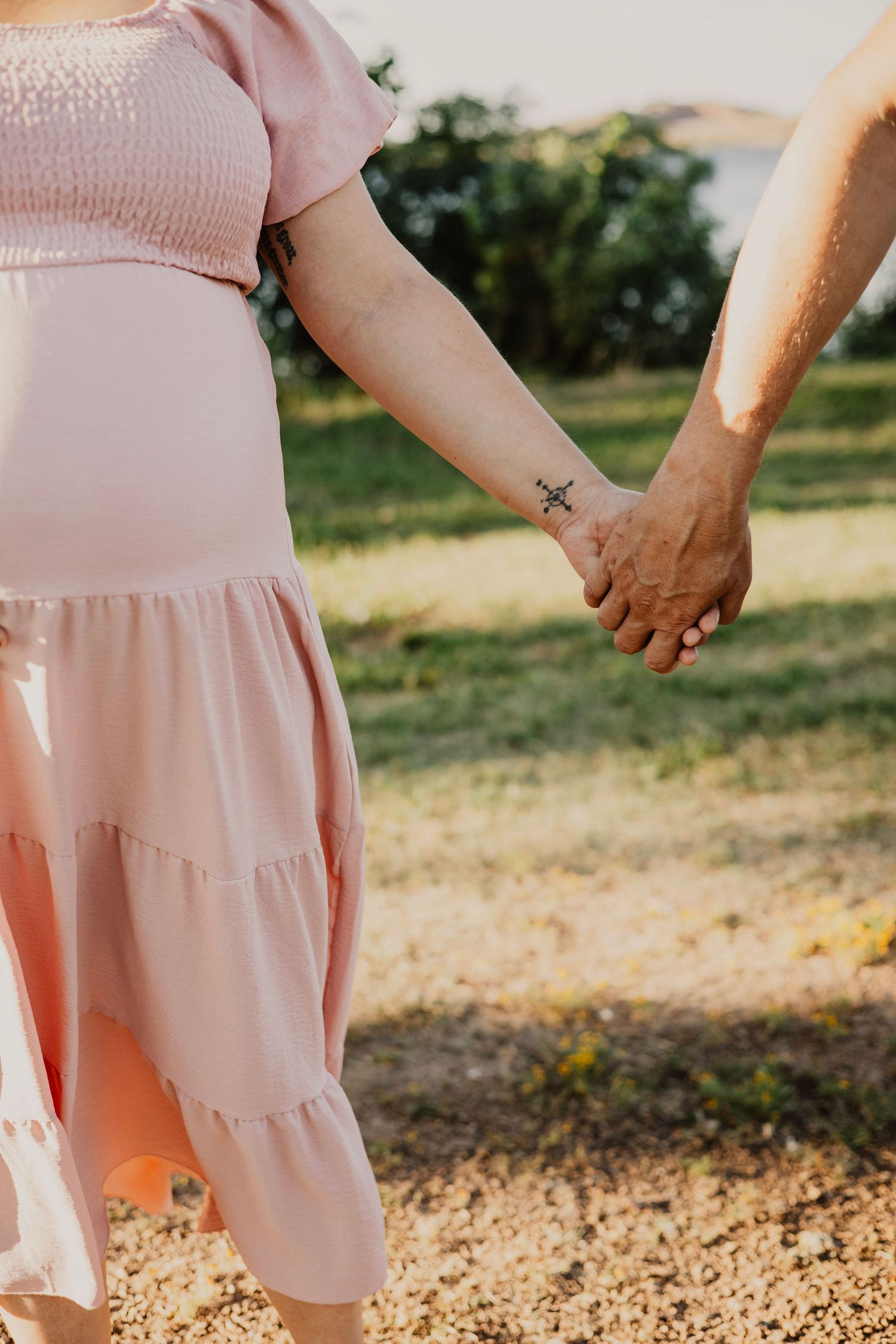 Couple holding hands in a field wearing pink and brown outfits during golden hour.