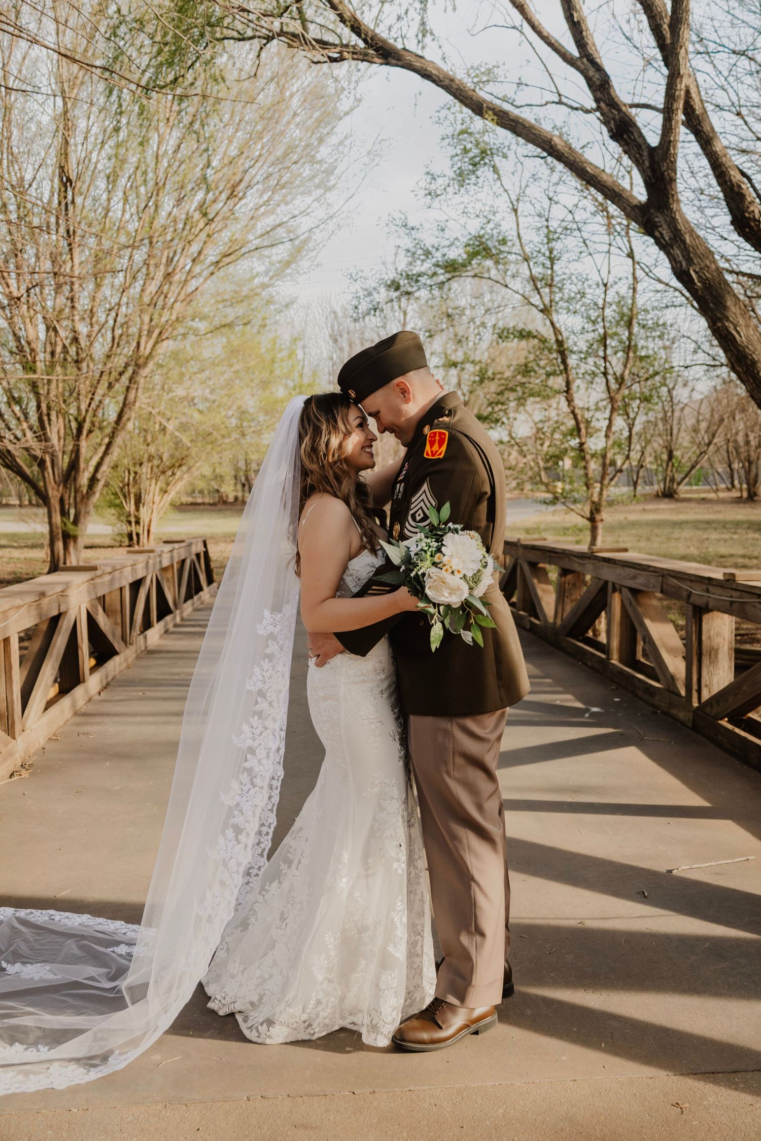 Wedding couple shares romantic moments on a wooden bridge in a park setting.