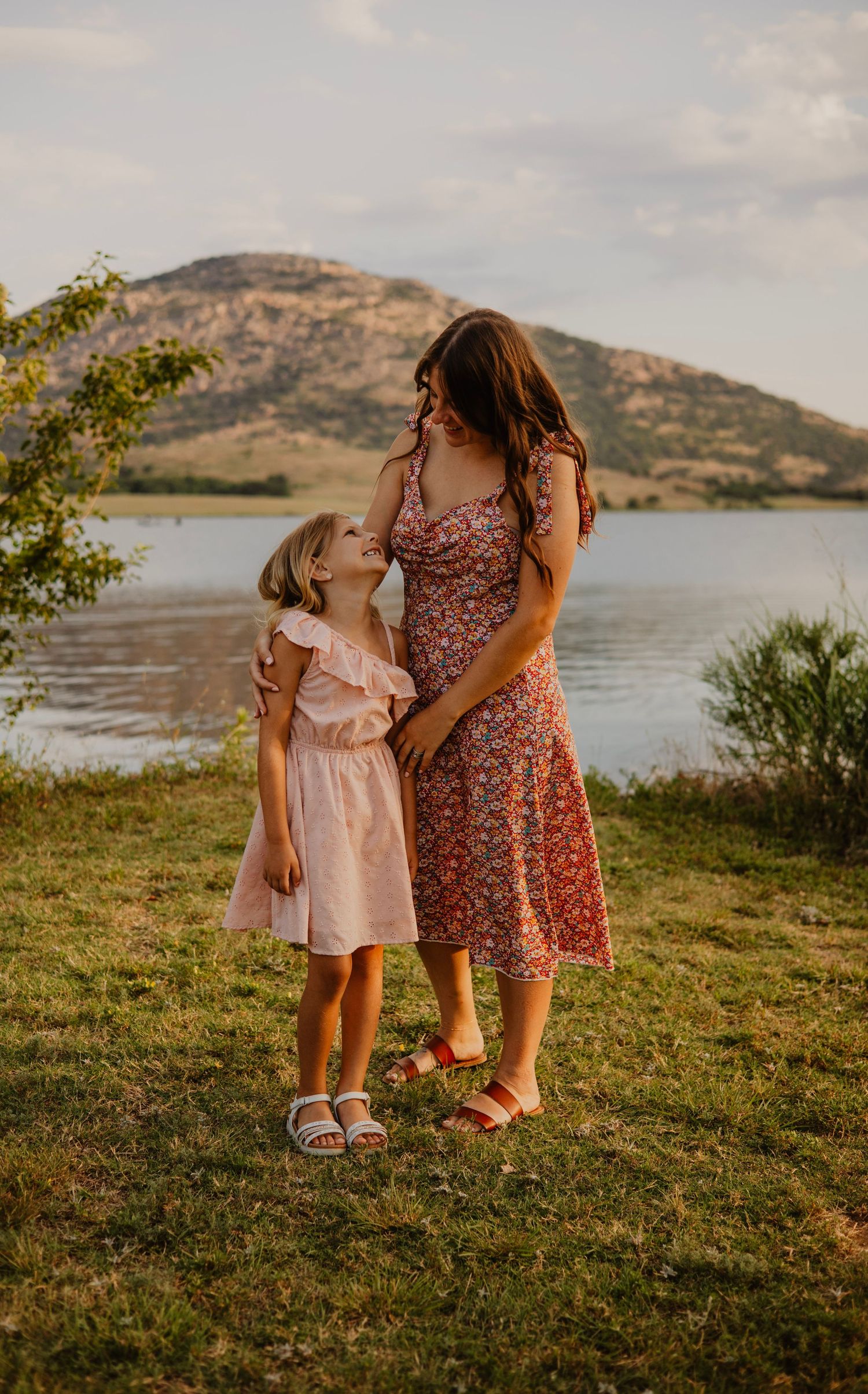 Mother and children interact playfully by lakeside with mountains in background.