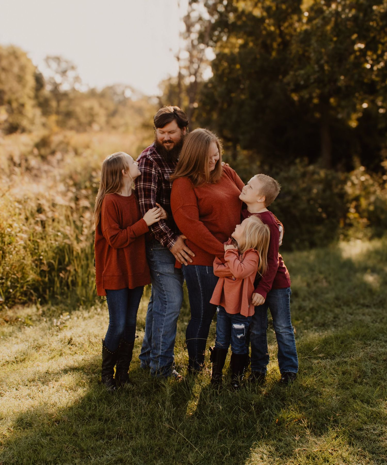 Family dressed in red and denim poses together in a golden sunlit field.