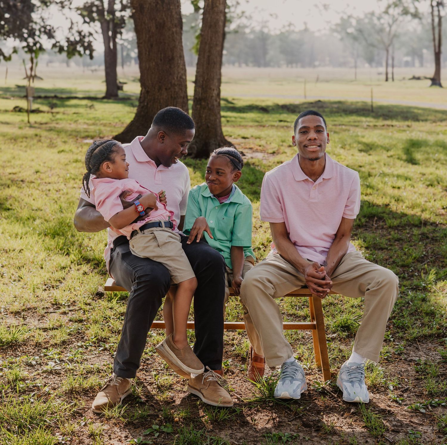 Family of four relaxes together under shady tree in grassy park setting.