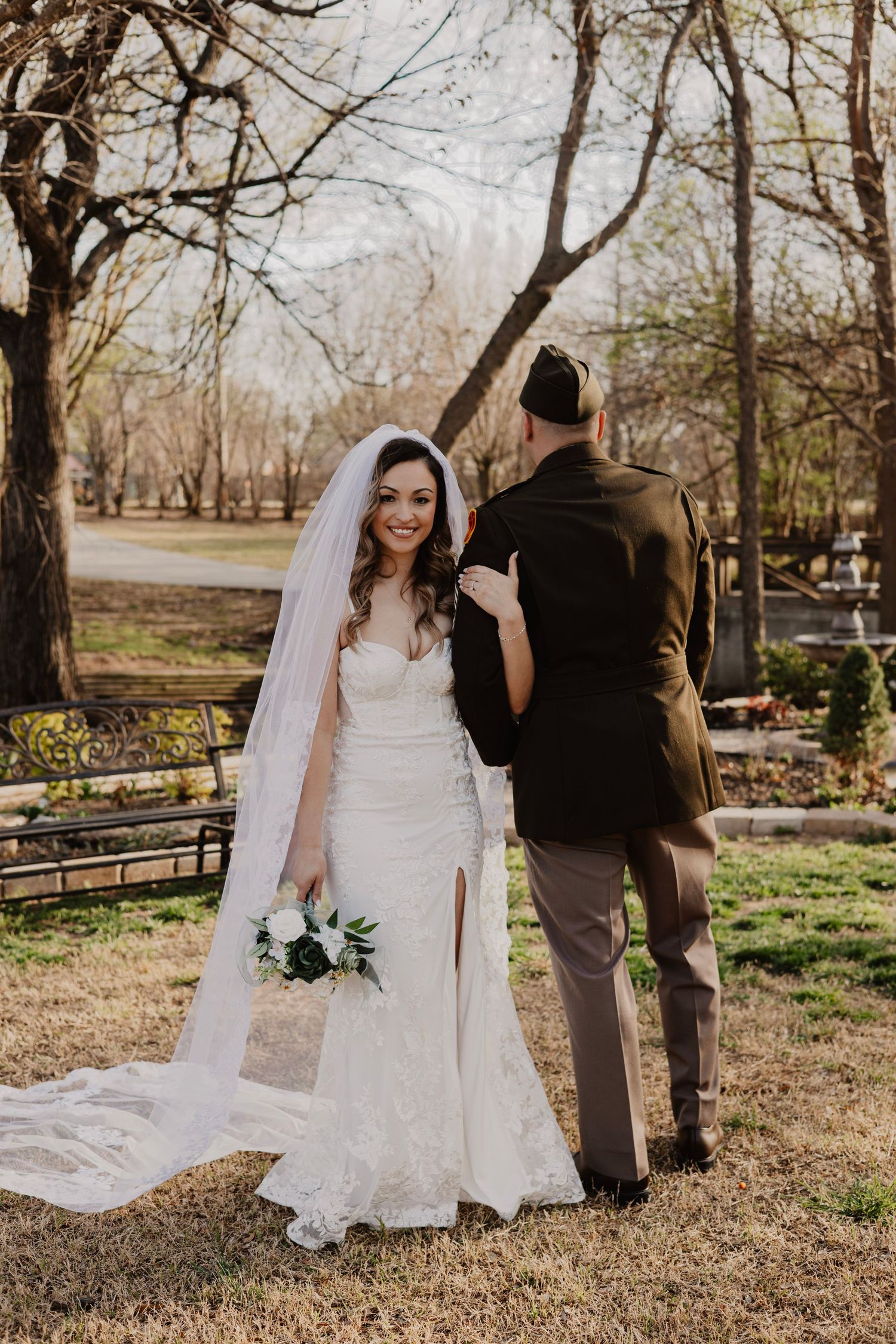 Wedding couple poses in a natural outdoor setting with bare trees and grass.