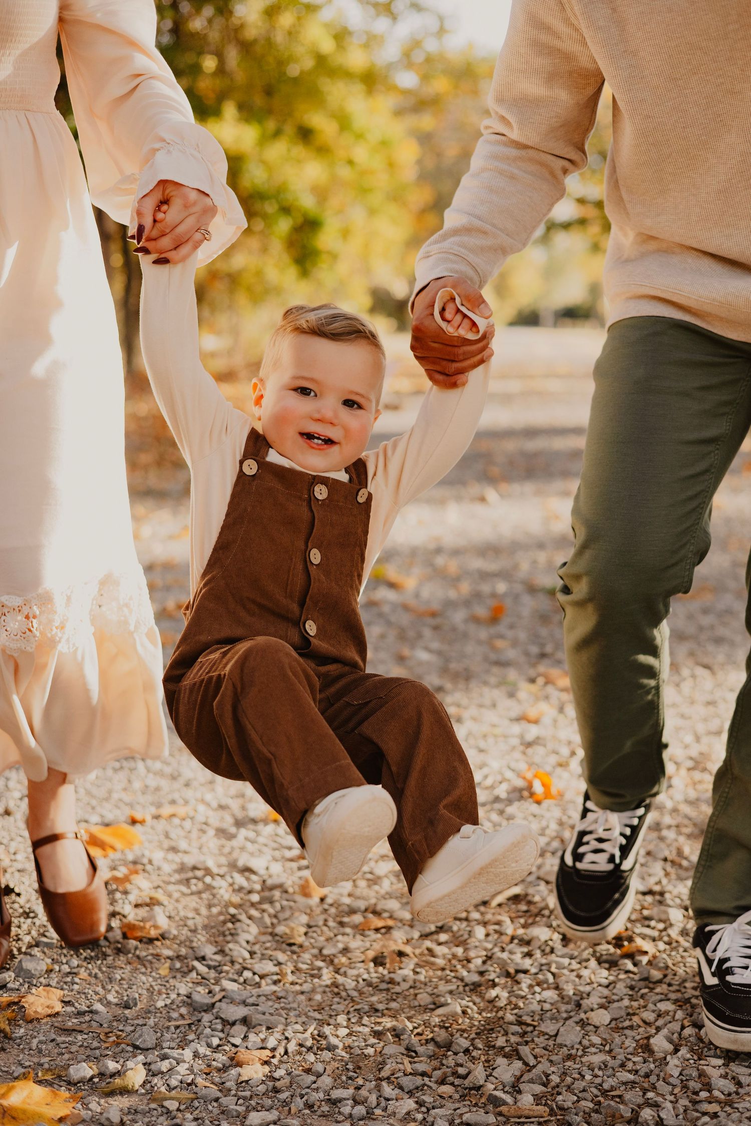 Small child swings joyfully between adults on autumn path.