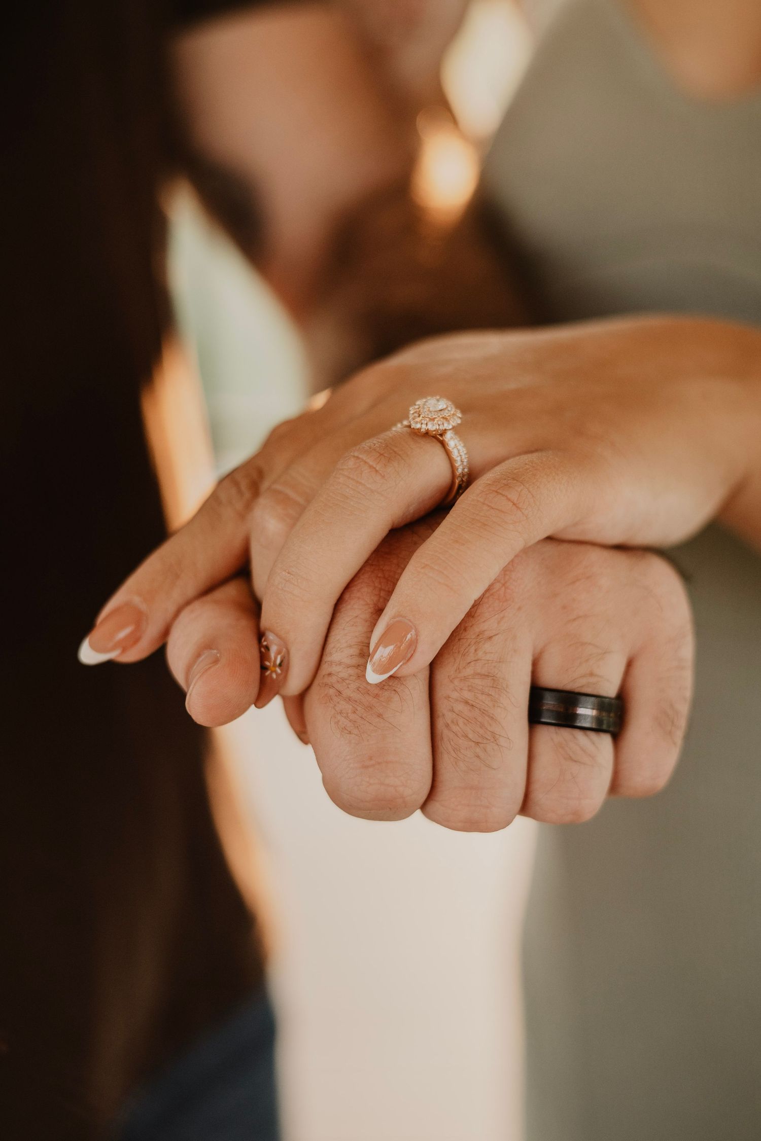 Close-up of hands with wedding rings showing a diamond engagement ring and black band in warm lighting.