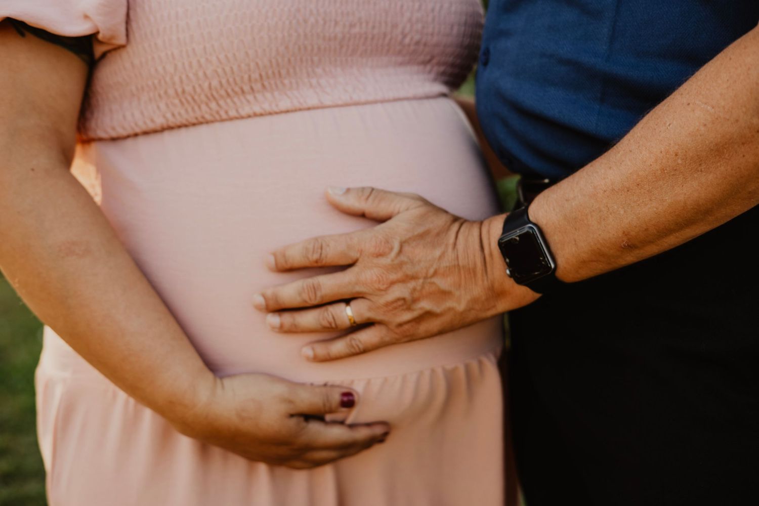 A close-up shot of hands tenderly cradling a pregnant belly in warm sunlight.