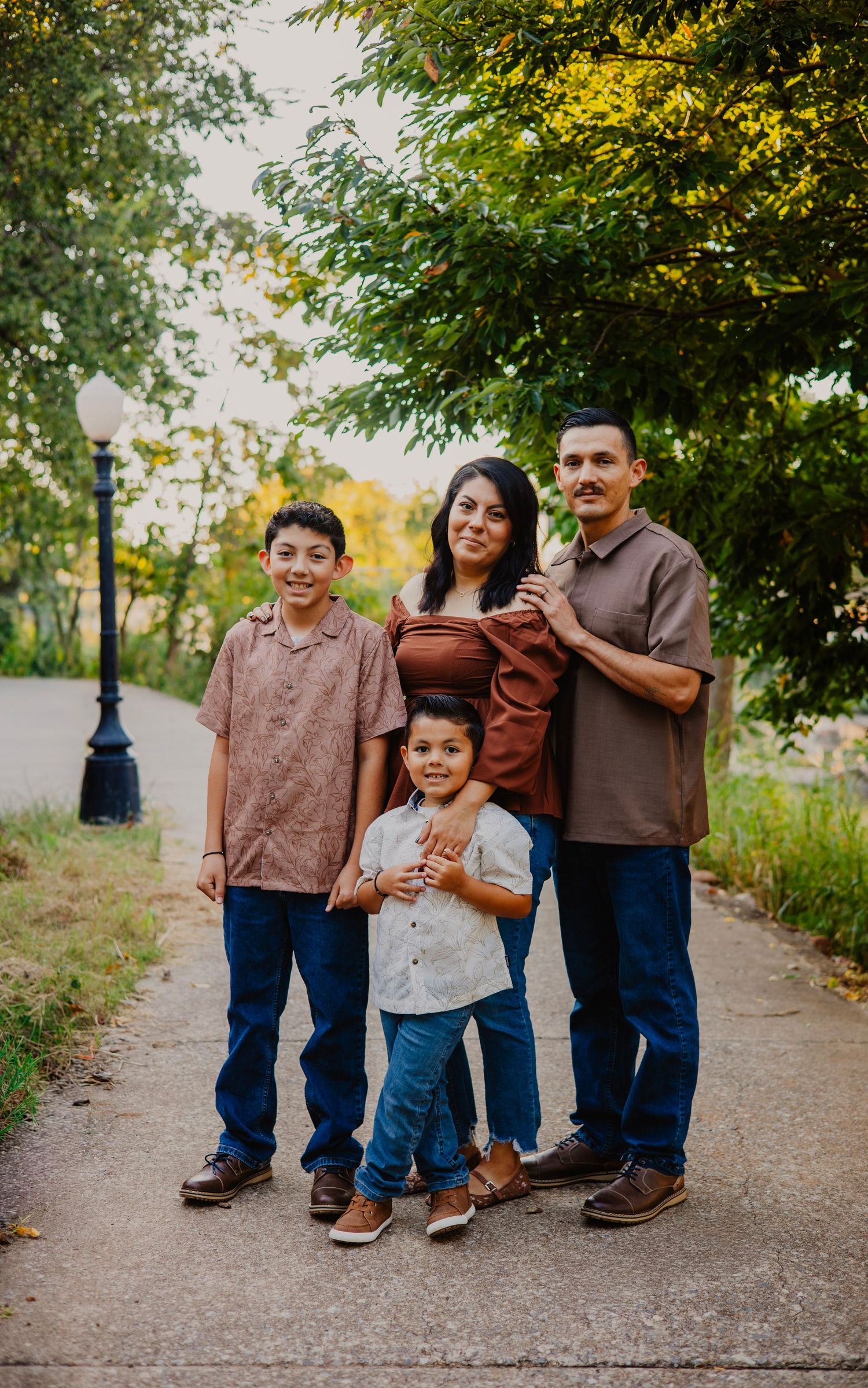 Family walks together on paved path under green trees wearing coordinated brown and blue outfits.