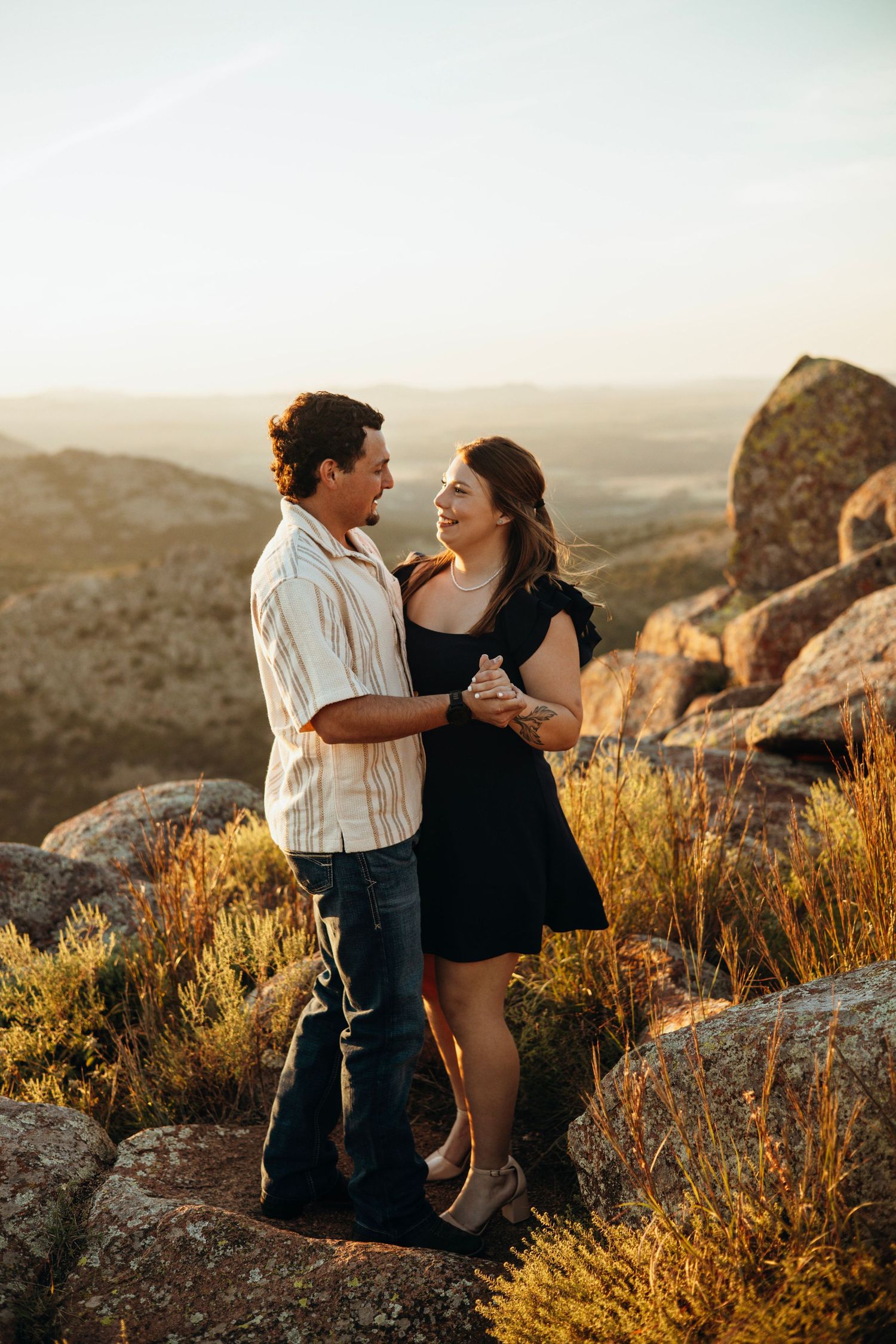 A romantic couple standing among desert rocks during golden hour.