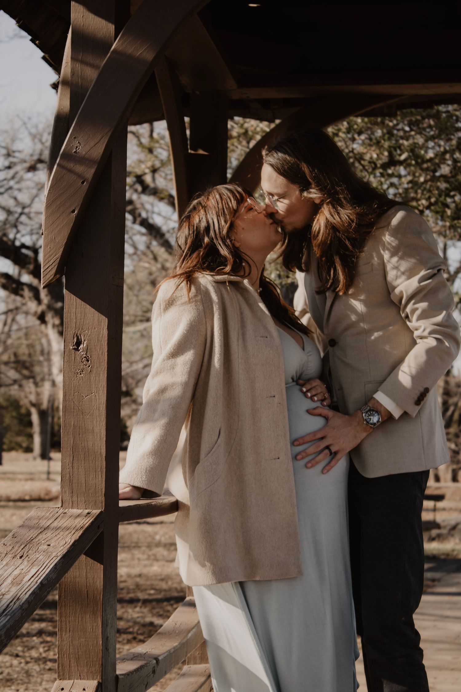 A couple shares a tender embrace under a wooden pergola during a romantic outdoor photo session.