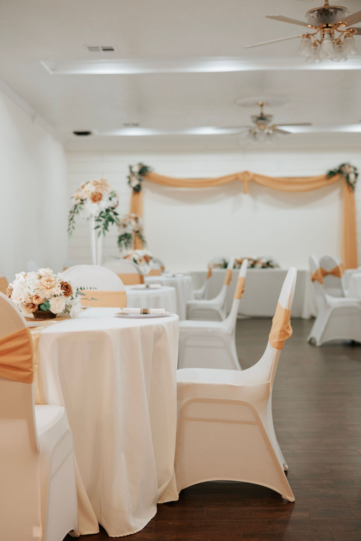 White tablecloth covered round tables with peach sashes in an elegant wedding reception venue.