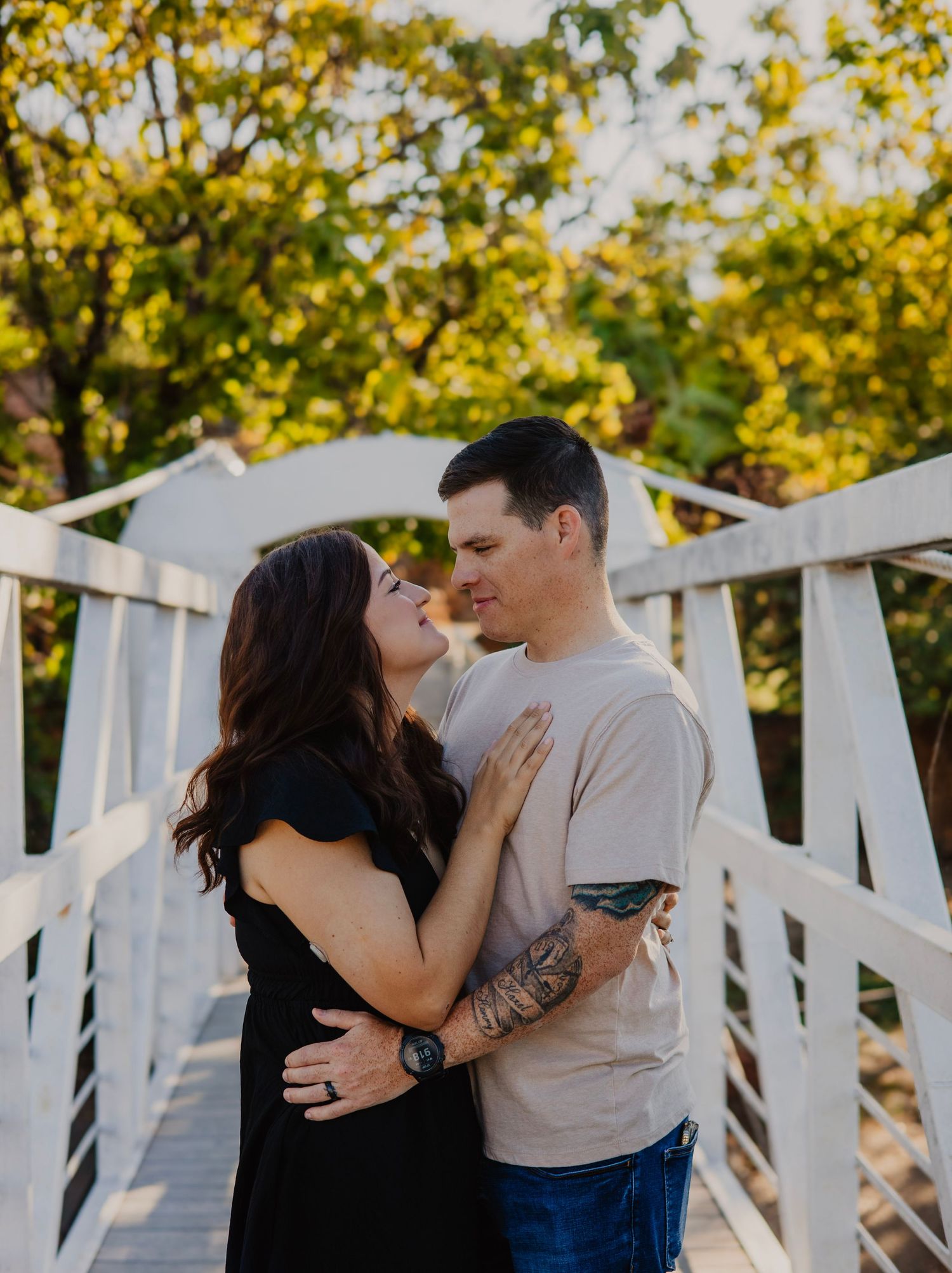A couple embracing on a white wooden bridge surrounded by autumn foliage.