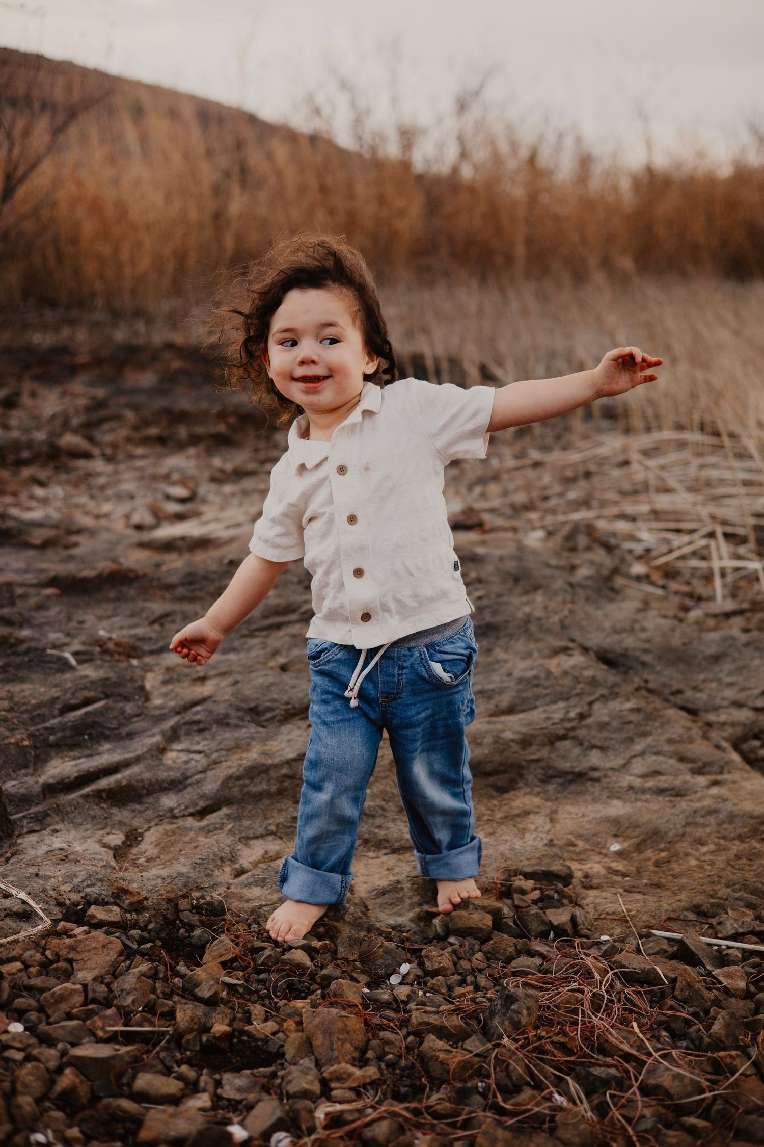 Young child plays joyfully outdoors in casual clothes on rocky terrain at sunset.