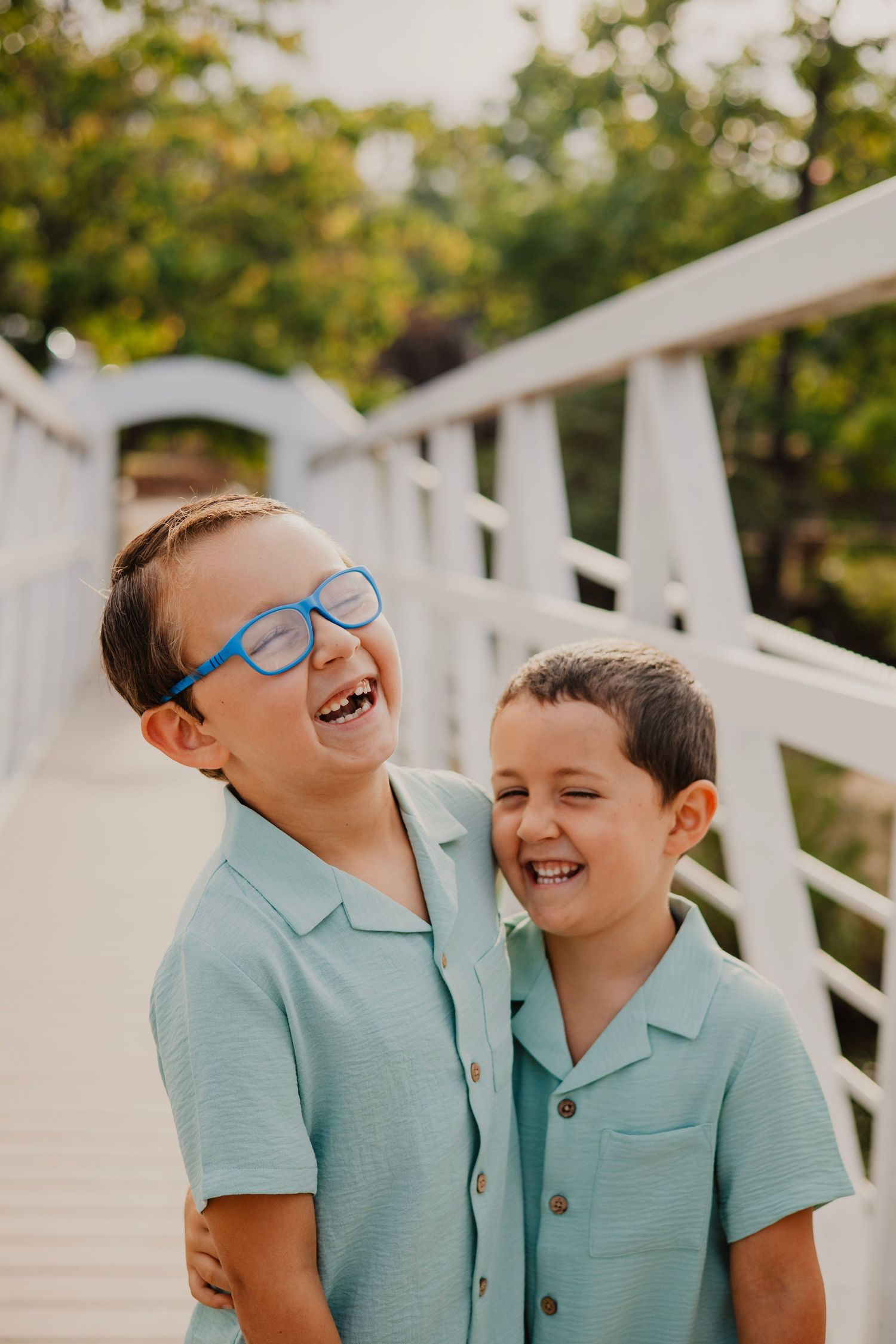 Two children in matching light blue polo shirts share a joyful laugh together on a white bridge.