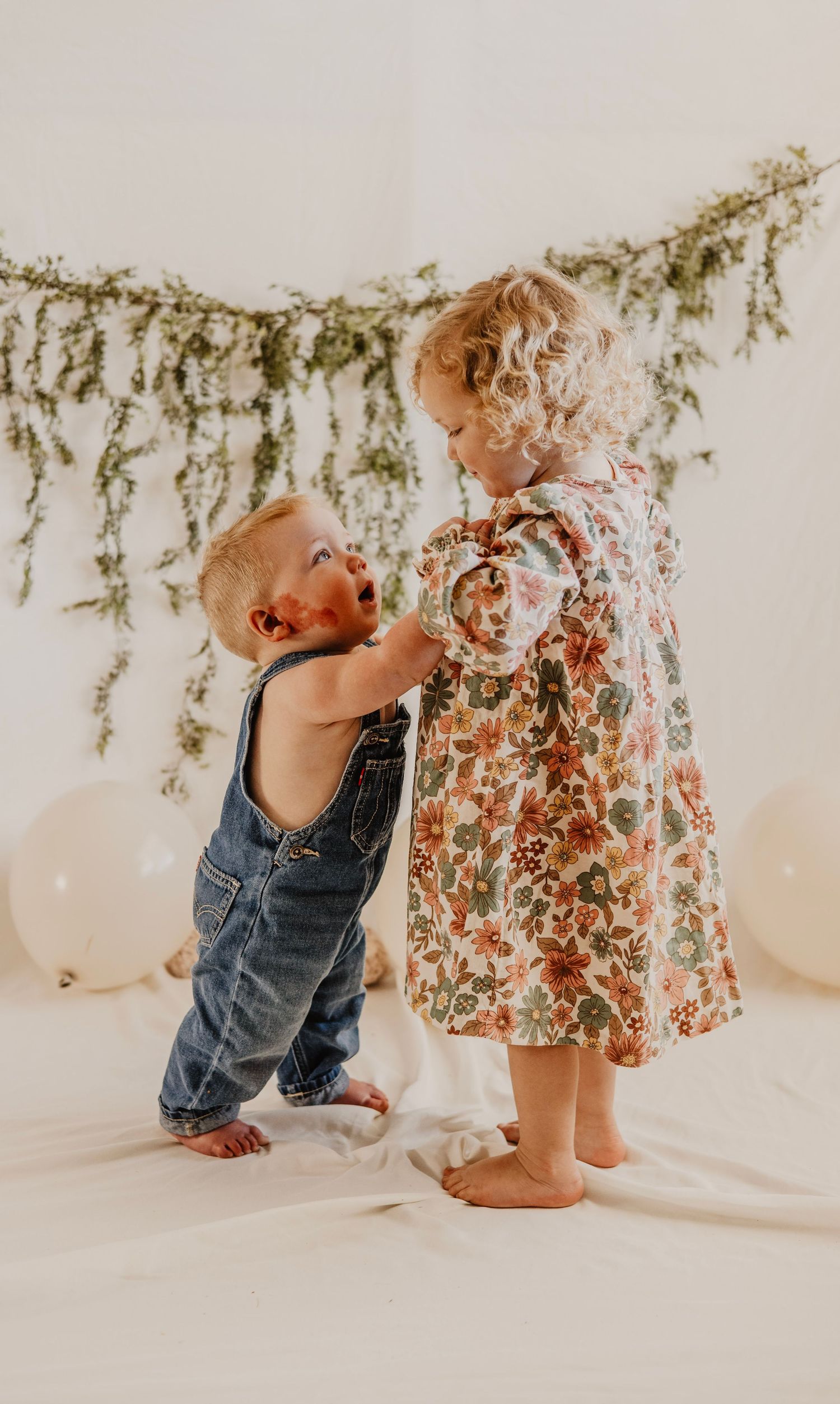 A baby in denim overalls crawls under a floral dress in a series of candid lifestyle photos.