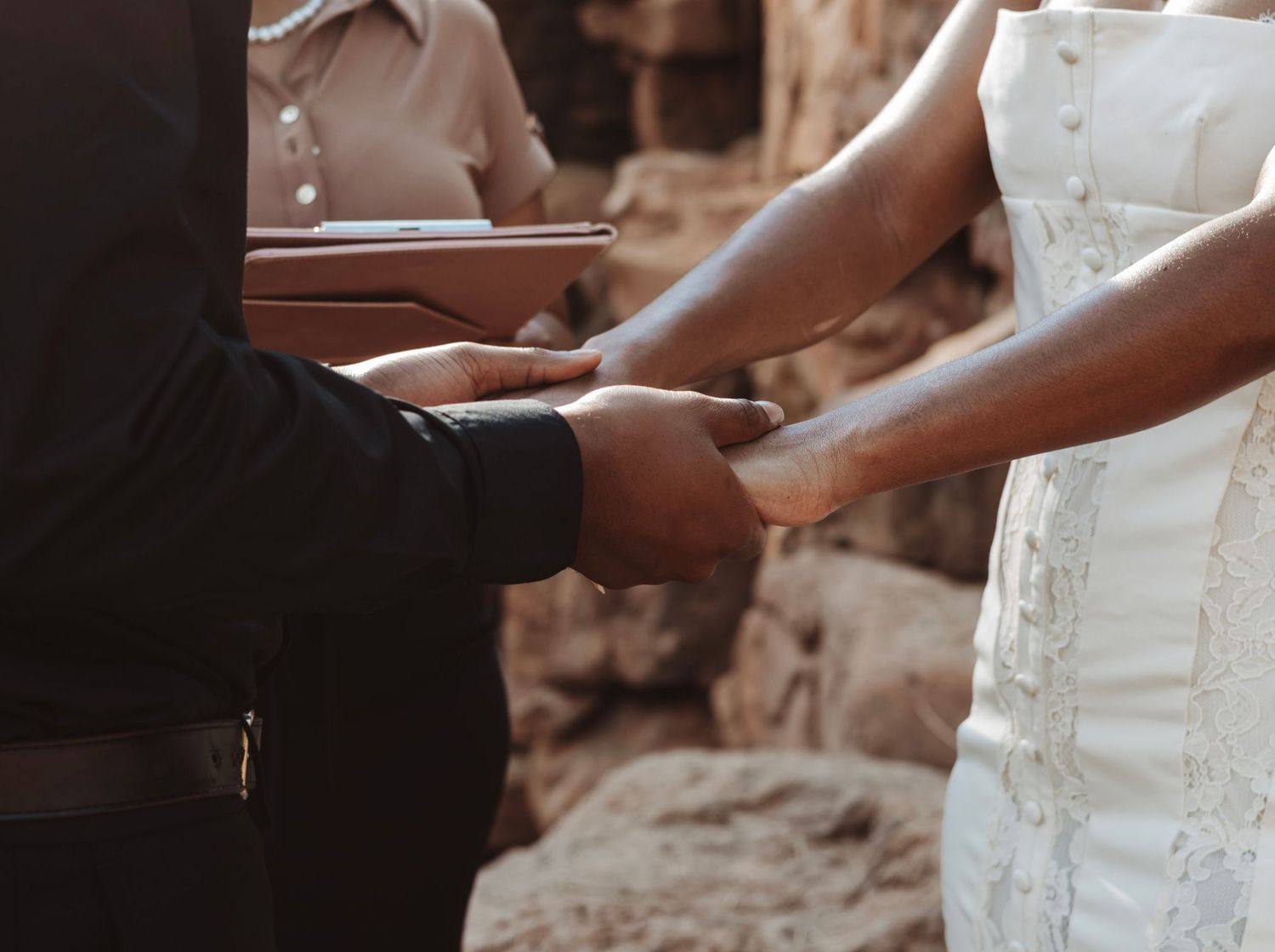 Wedding couple holding hands with focus on white lace dress details.