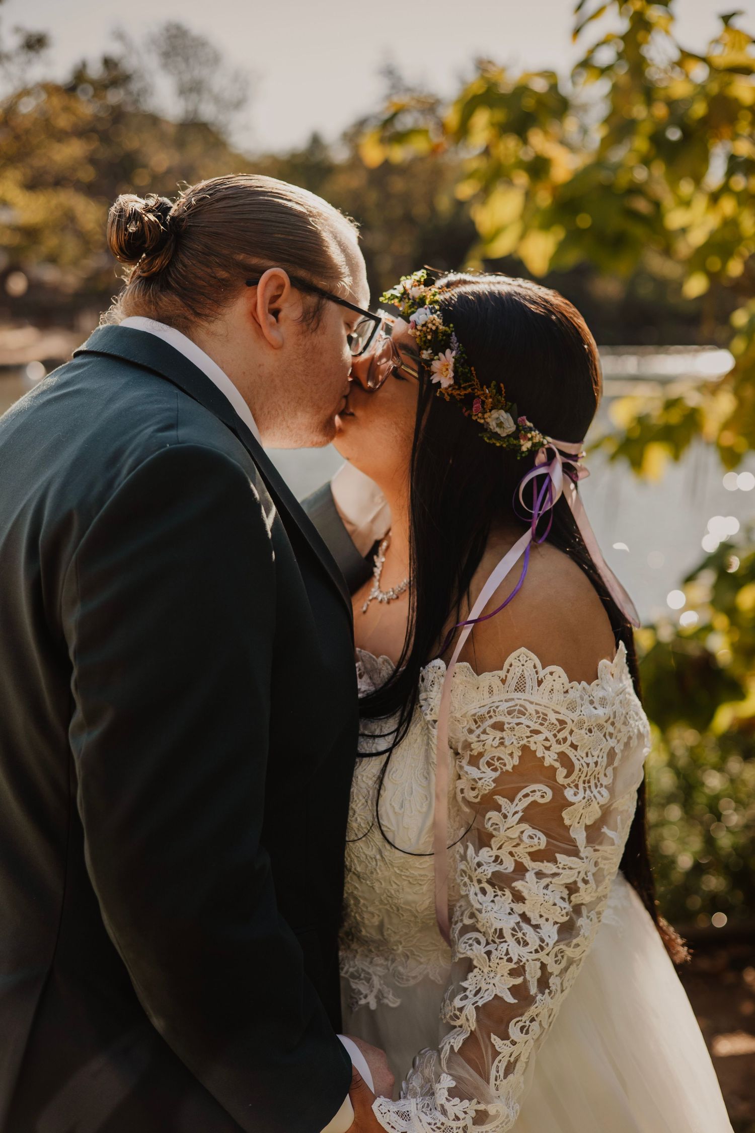 Wedding couple shares intimate moment in golden sunlight with detailed lace dress visible.