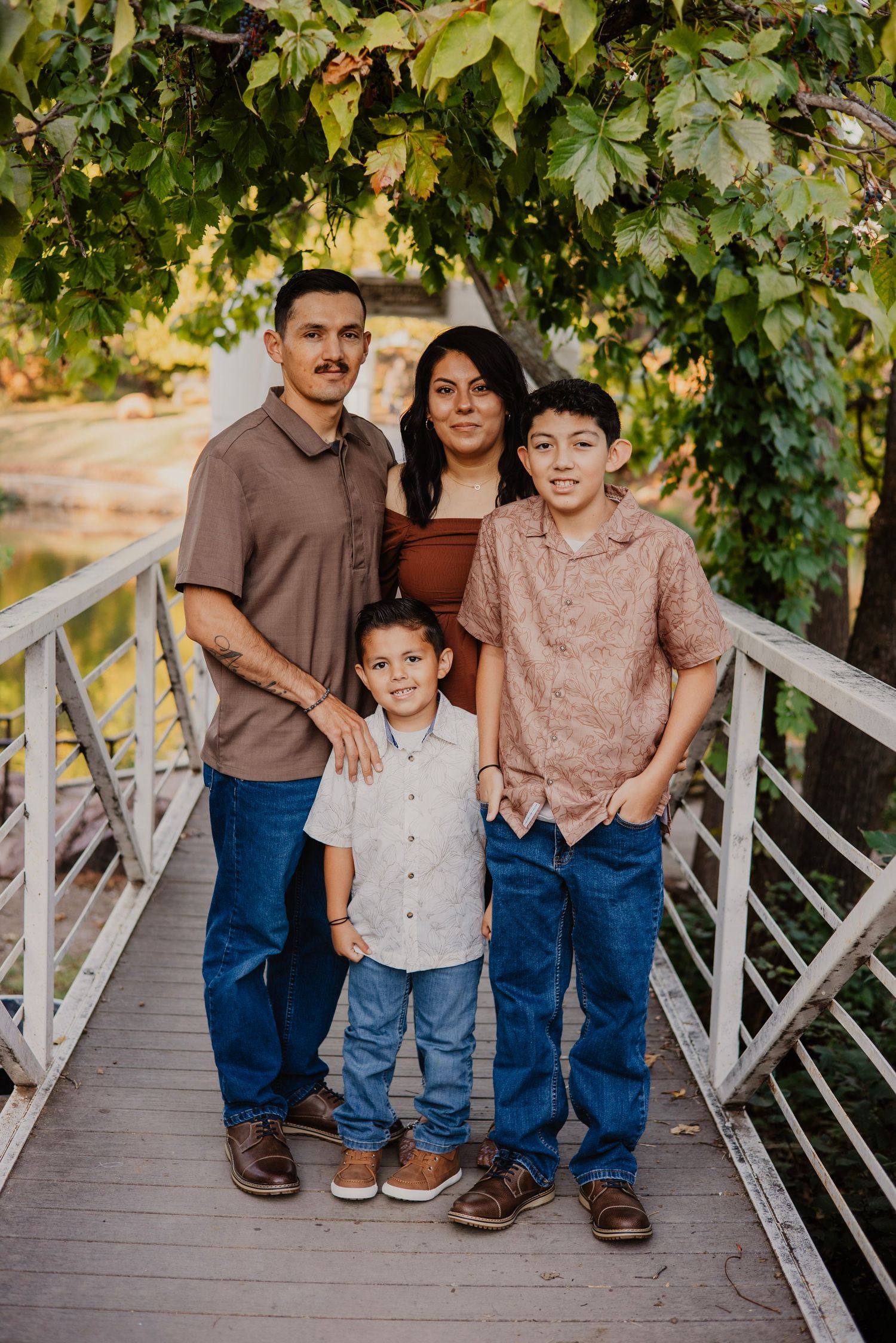 Family poses on wooden bridge under green foliage in coordinated casual outfits.