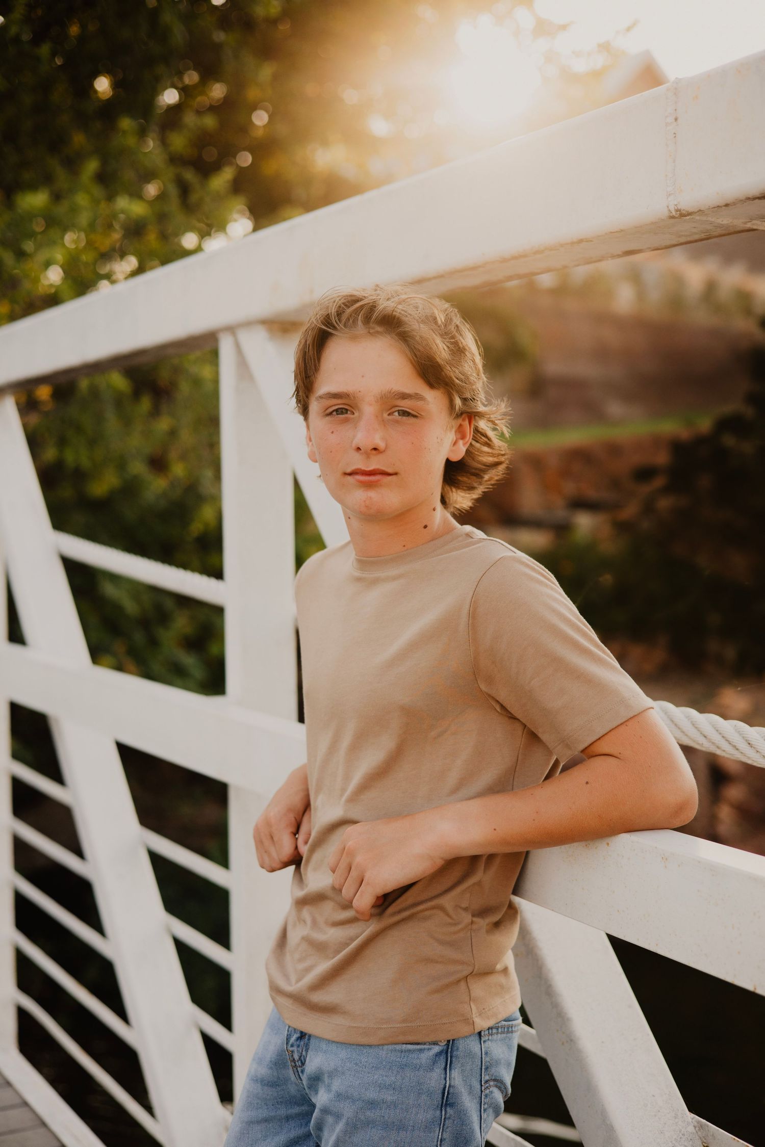 Youth in casual attire poses along white railing during golden hour photoshoot.