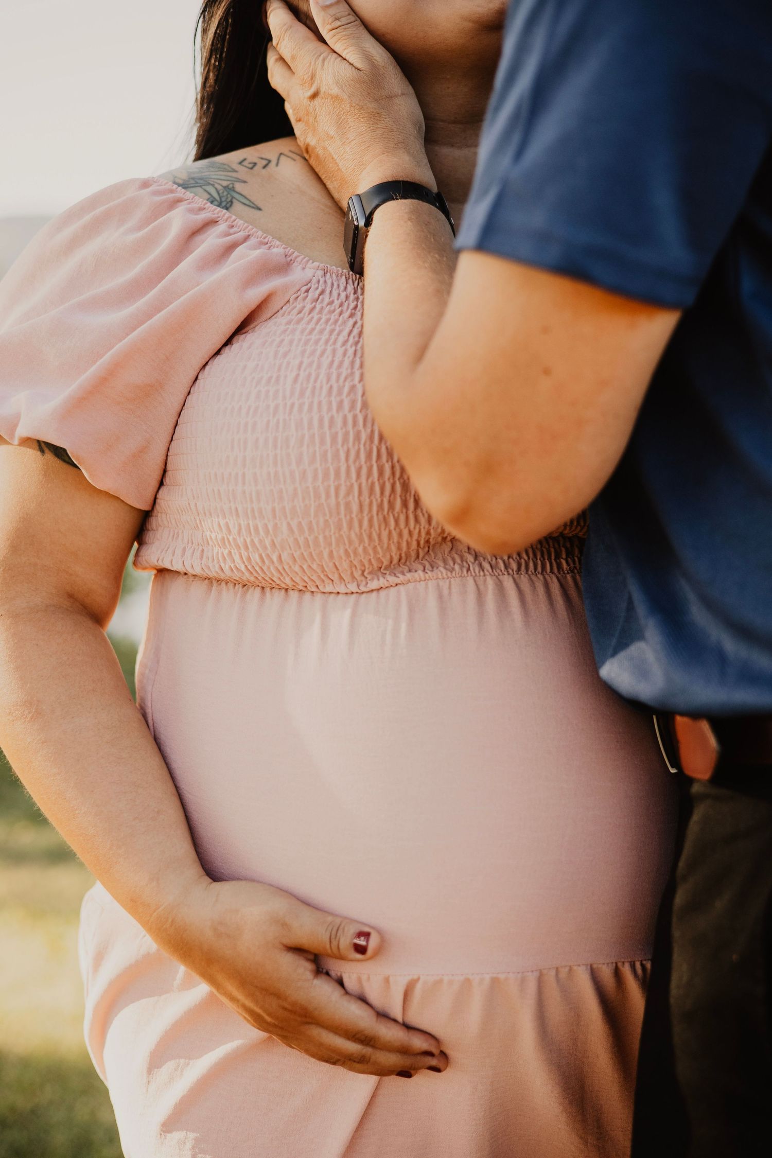Close up of hands tenderly touching a pink maternity dress.