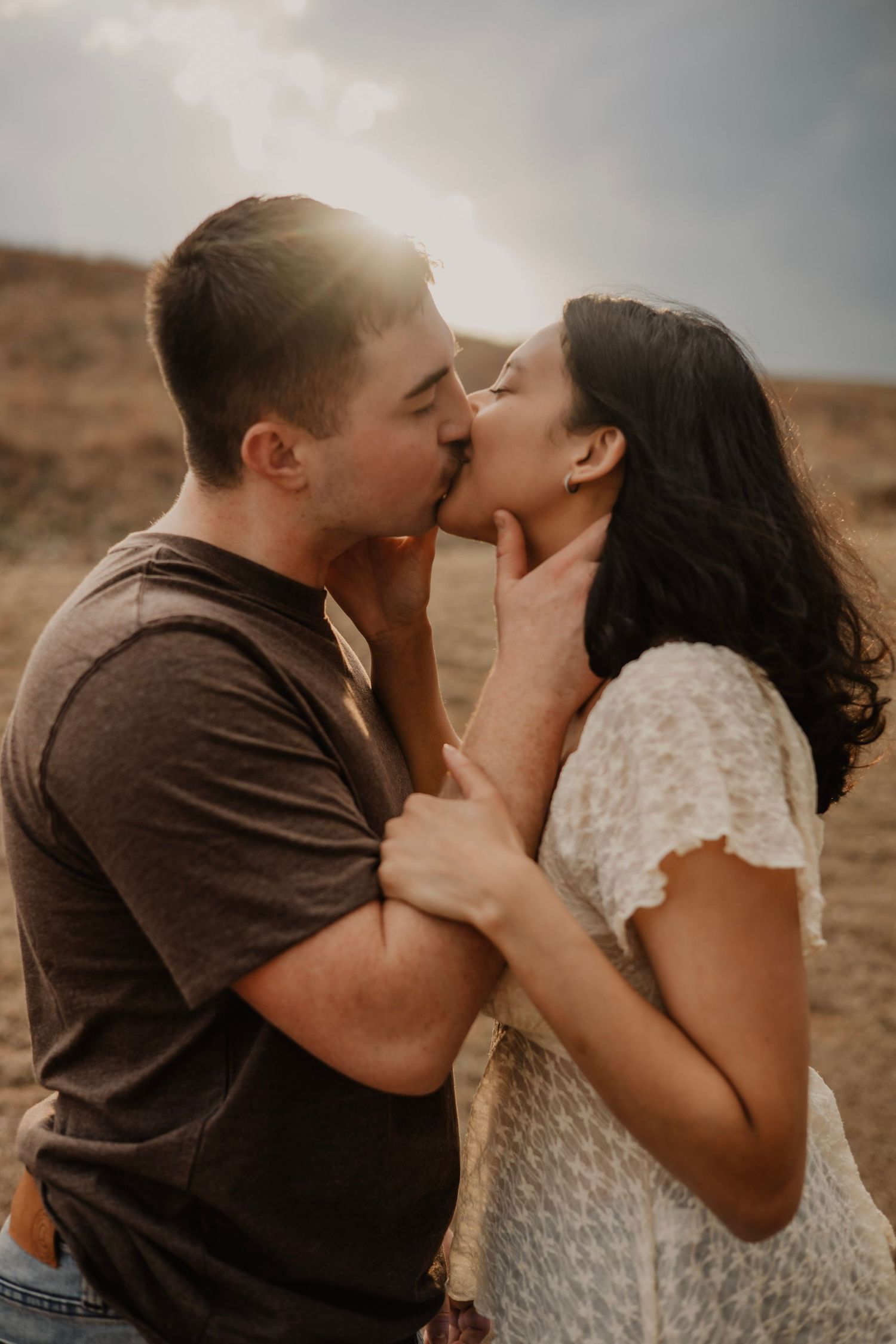 An intimate moment between a couple sharing a kiss during golden hour in a desert setting.
