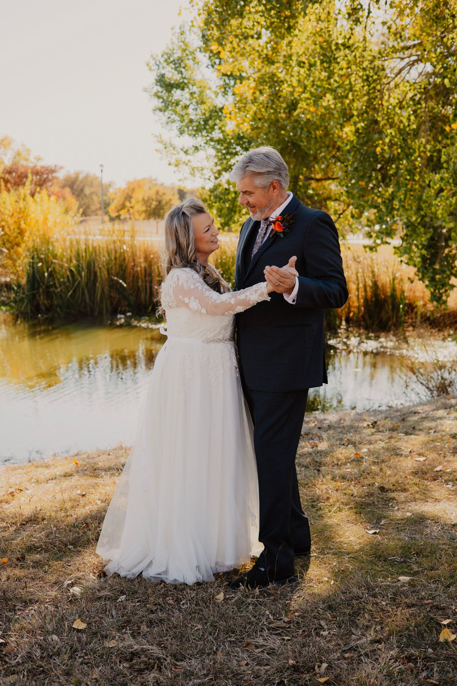 Wedding couple posing by a lake with autumn trees creating a romantic outdoor setting.