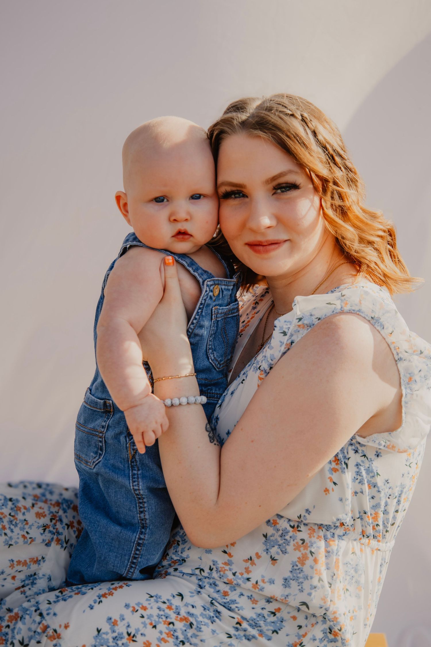 Intimate portrait session with parent and baby in floral dress against neutral backdrop.