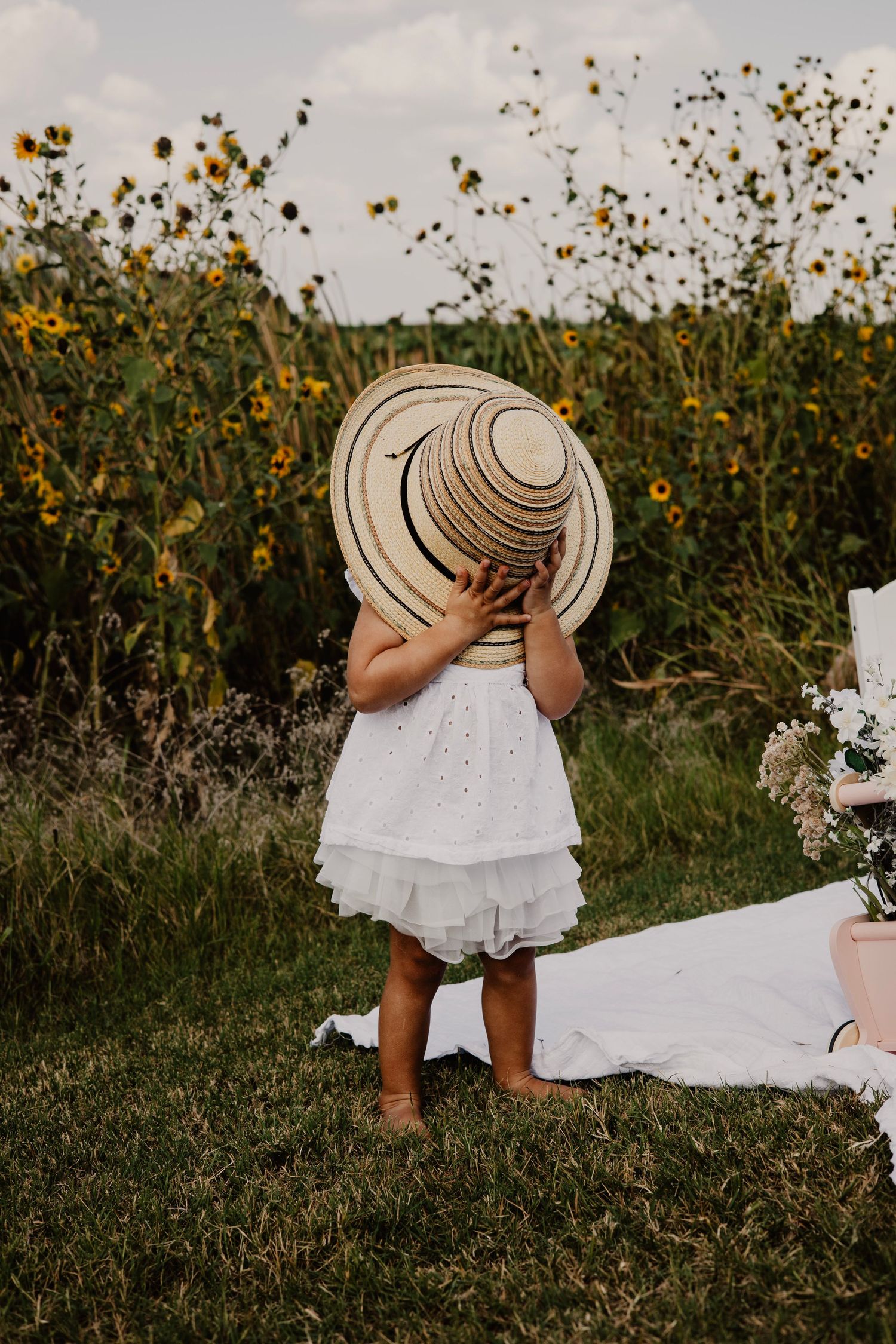 A white dress and brown boots stand in a wildflower meadow with yellow blooms on a sunny day.