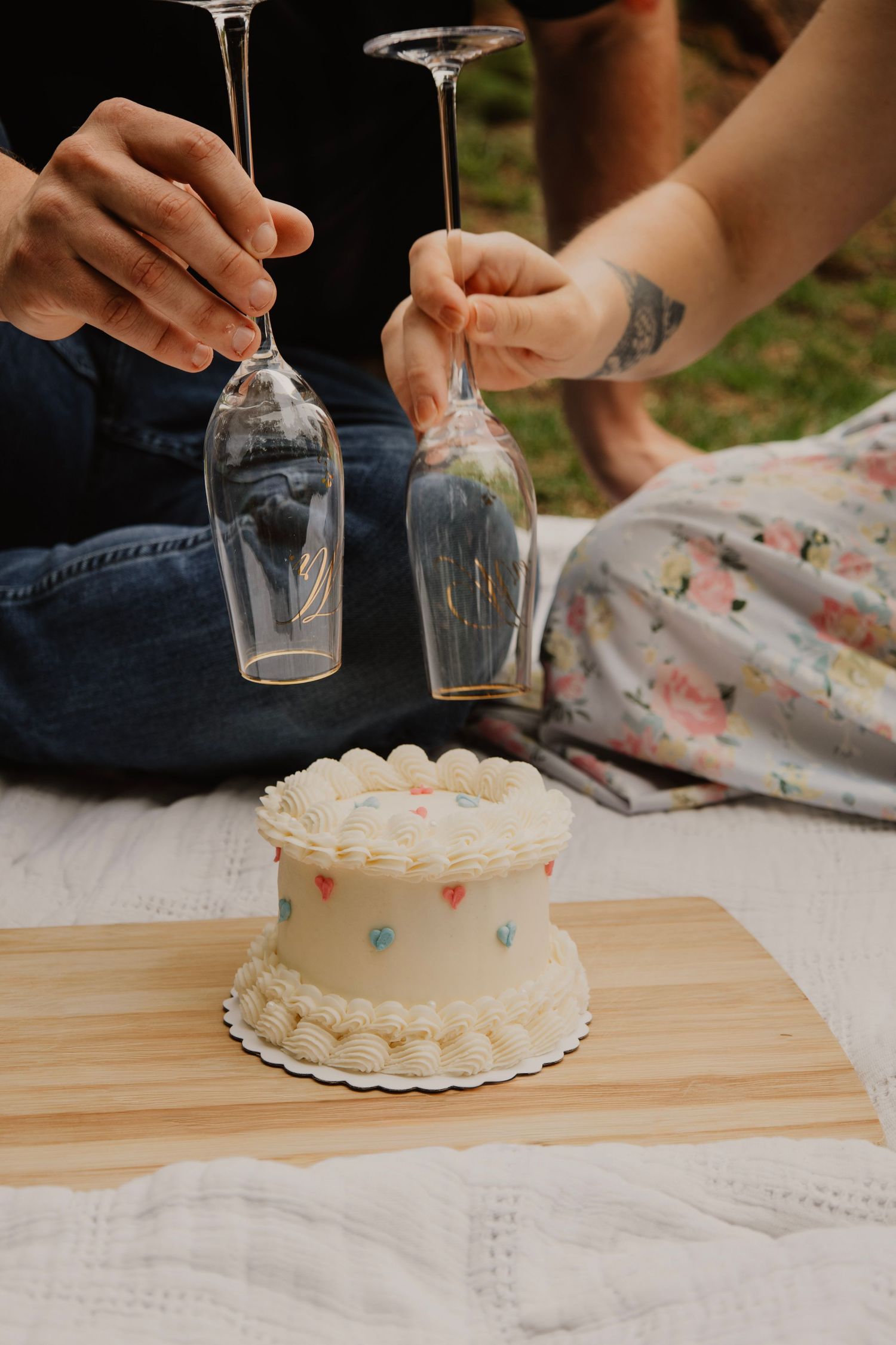 Two hands holding wine glasses over a small white cake with pastel decorations.
