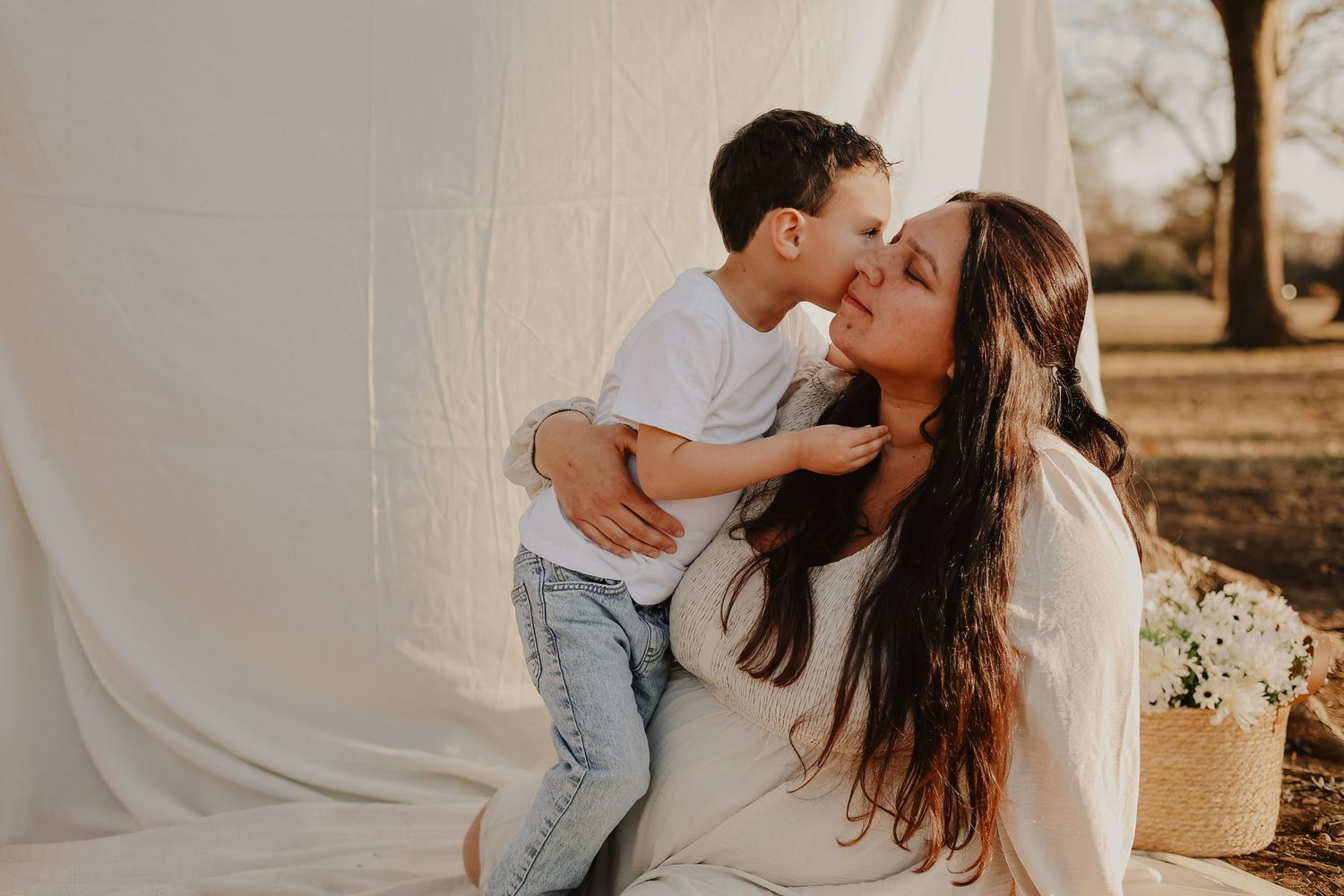 Mother and child share affectionate moment against white backdrop with natural lighting.
