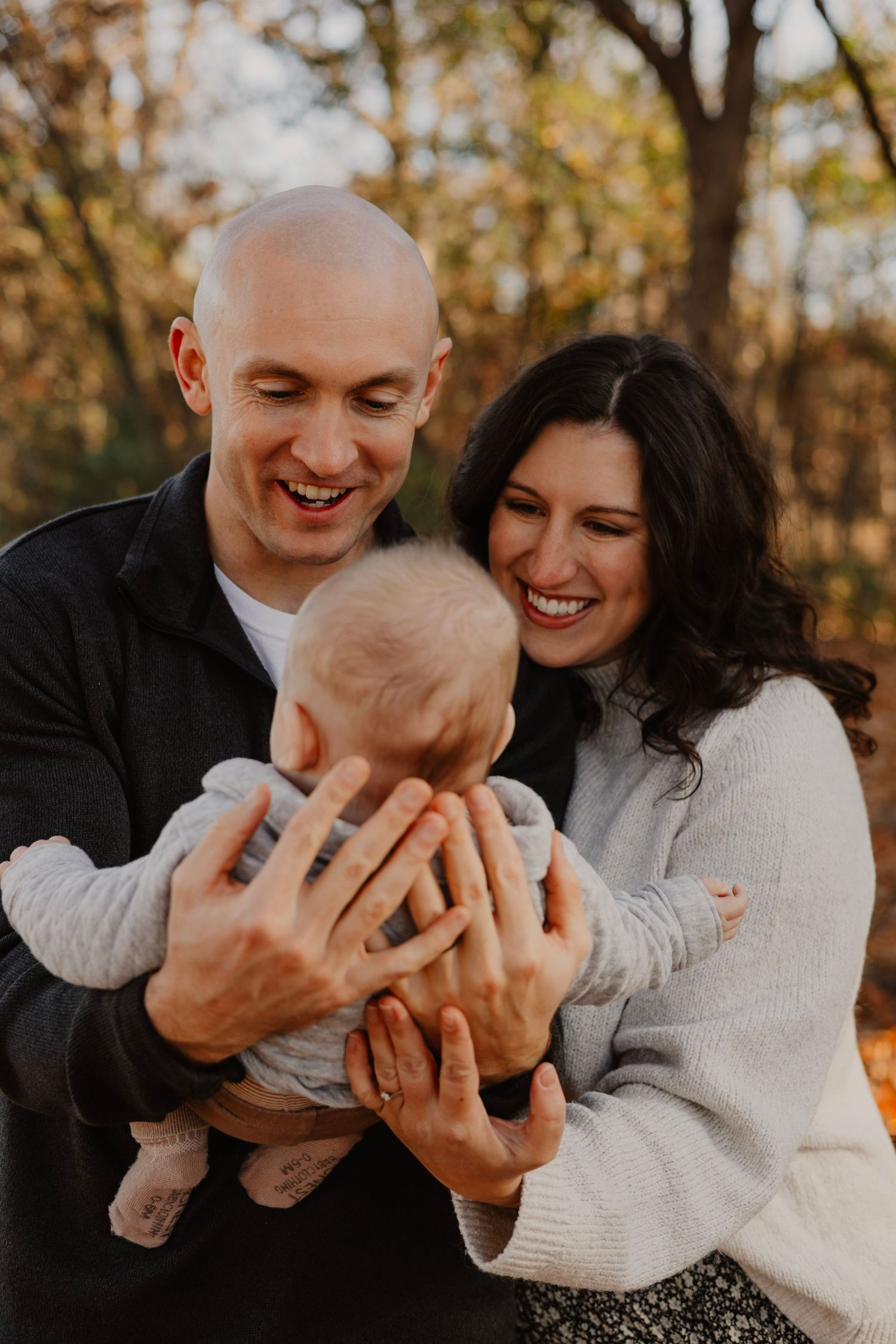 A couple in white sweaters shares intimate playful moments during a fall outdoor photoshoot with golden autumn trees in background.