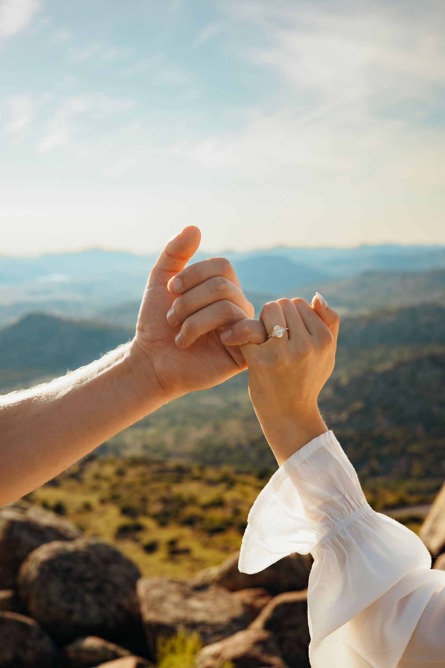 Two hands making a pinky promise against a scenic mountain backdrop.