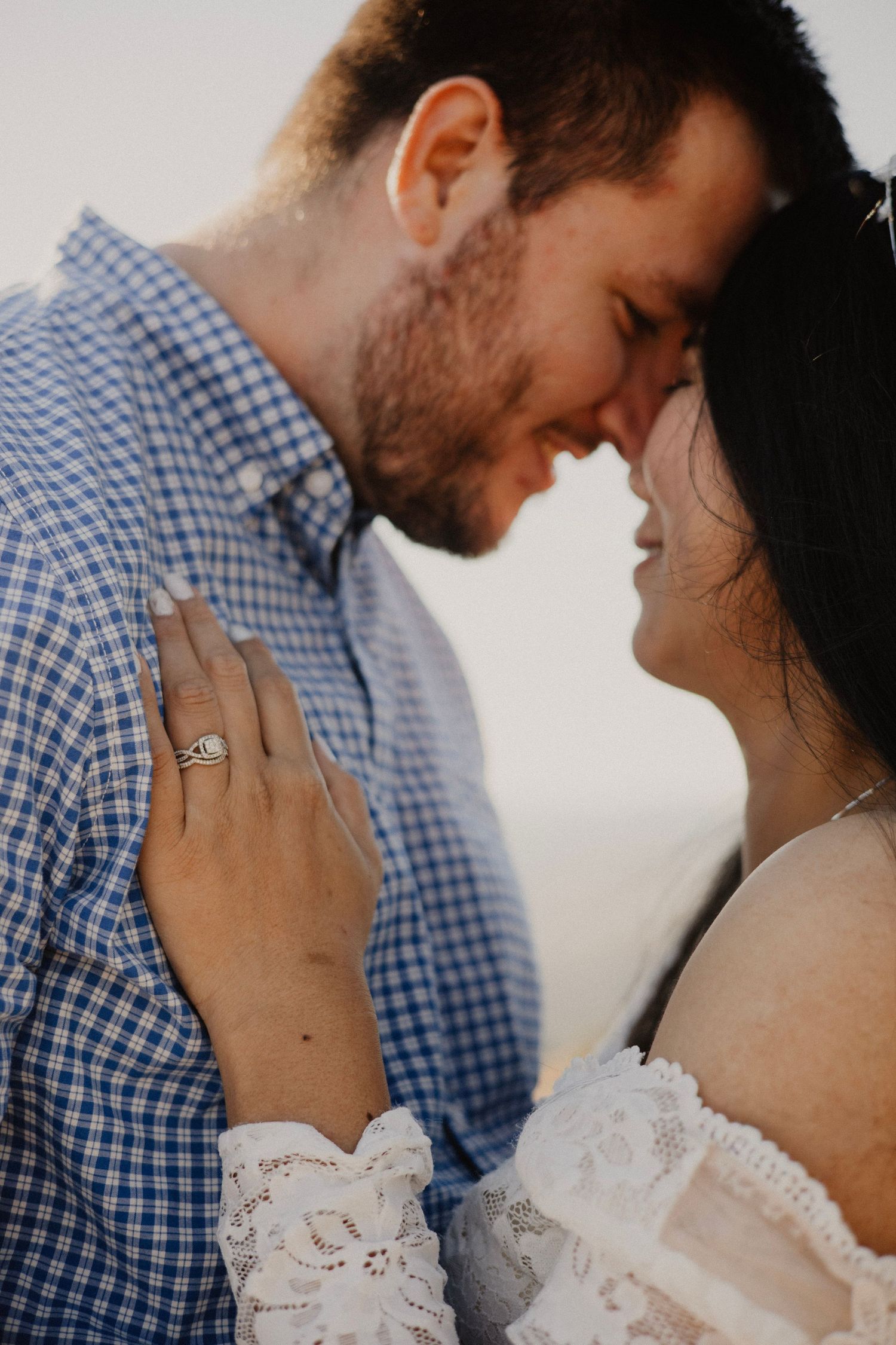 An intimate moment between a couple showing an engagement ring and lace sleeve details.