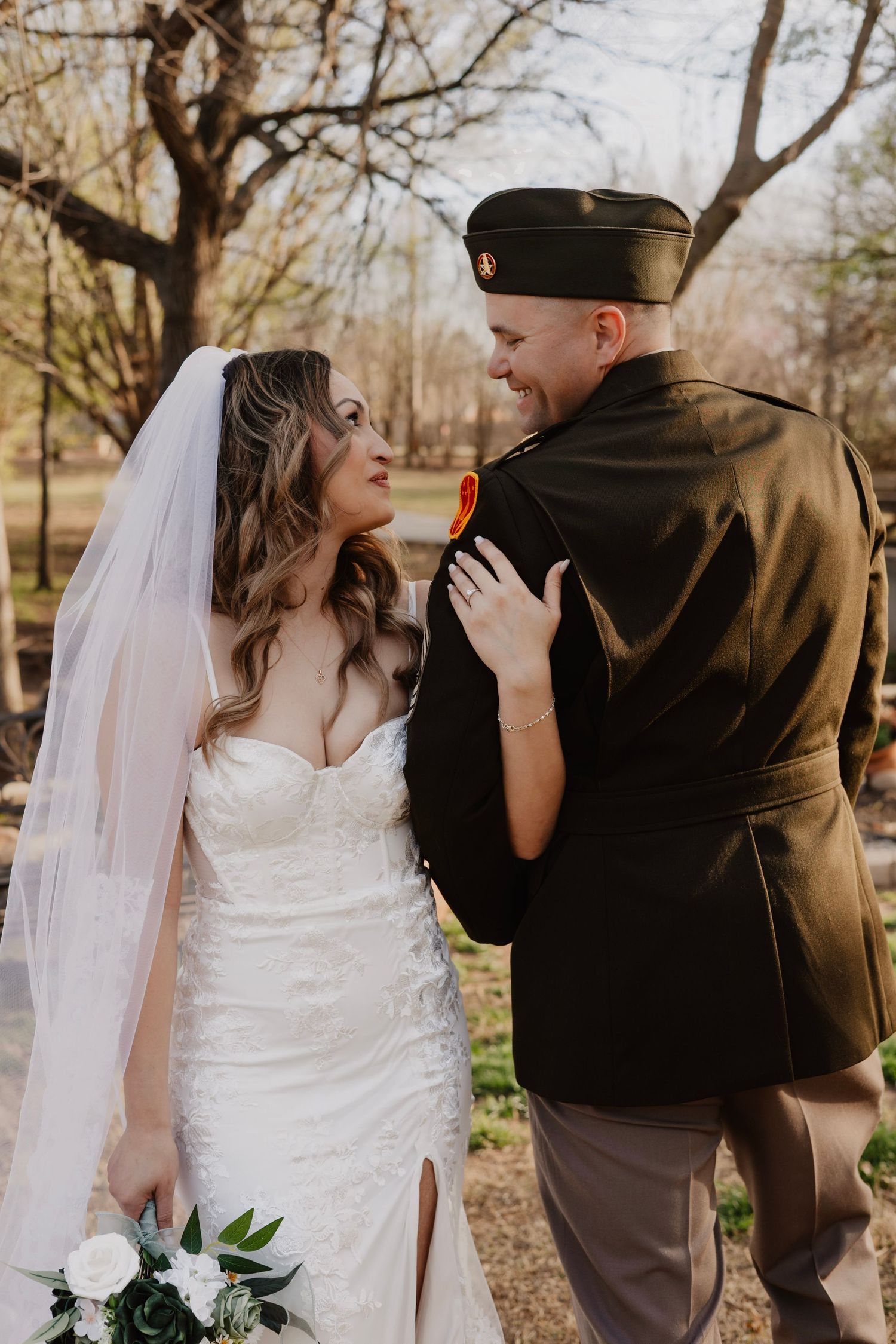 A bride in white dress and groom in military uniform share intimate moments outdoors in autumn.