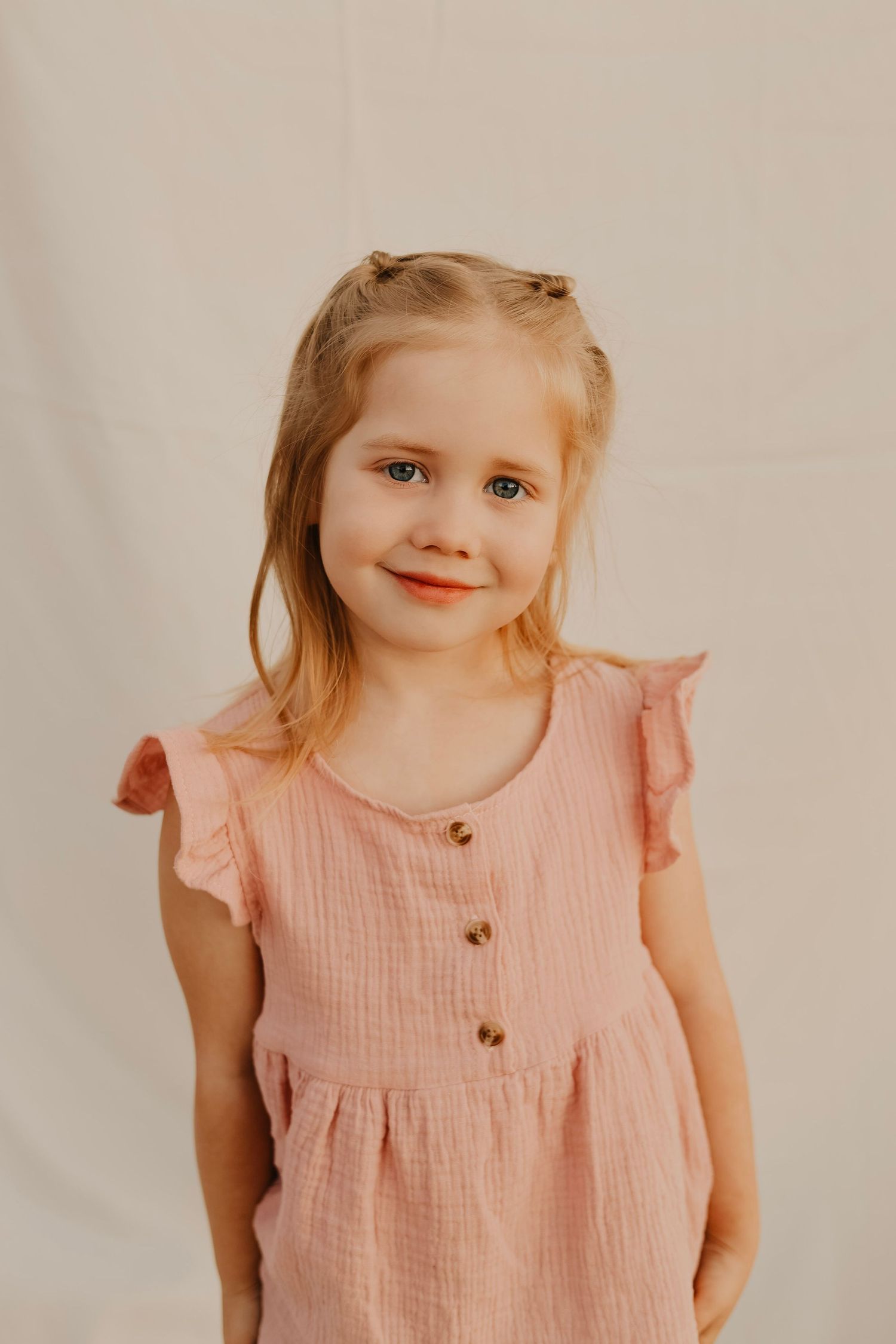 Little one wearing pink ruffled dress smiles sweetly in series of candid portrait shots.