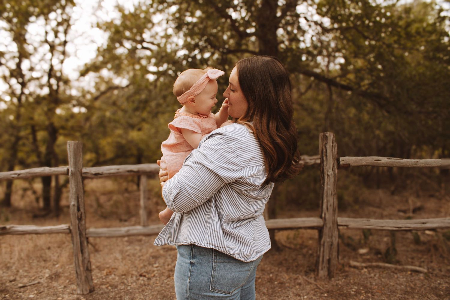 Mother and baby share tender moment by rustic wooden fence at sunset.