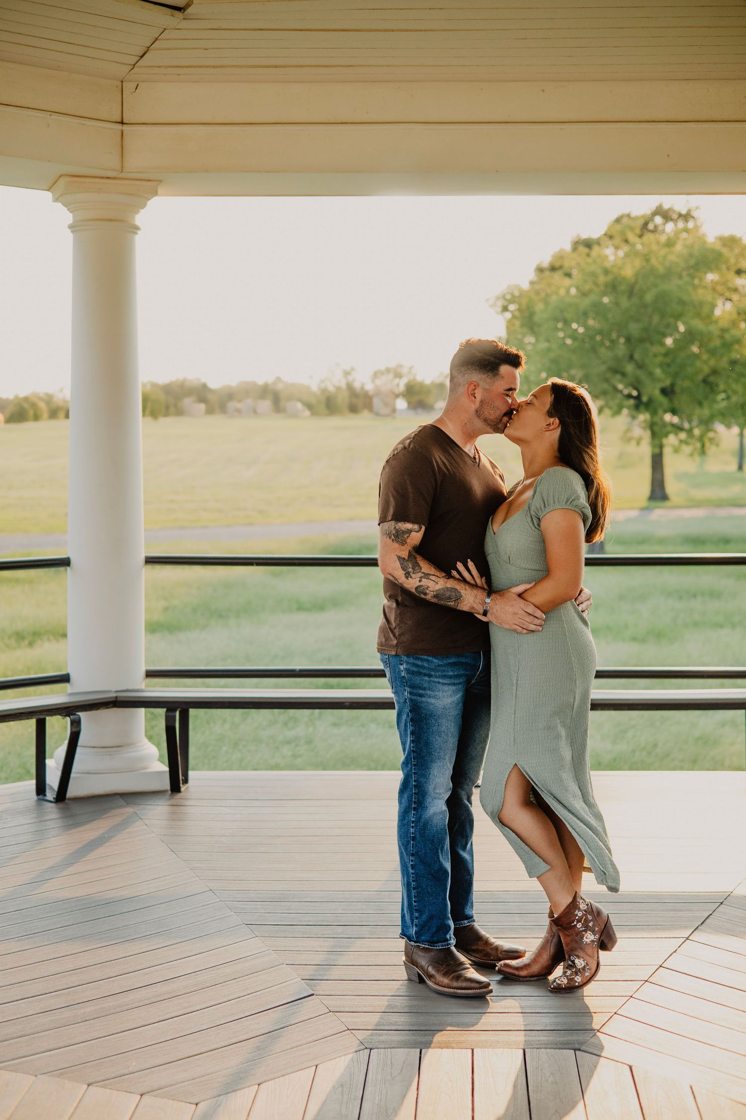 Couple sharing romantic moment on white porch with countryside view at sunset.