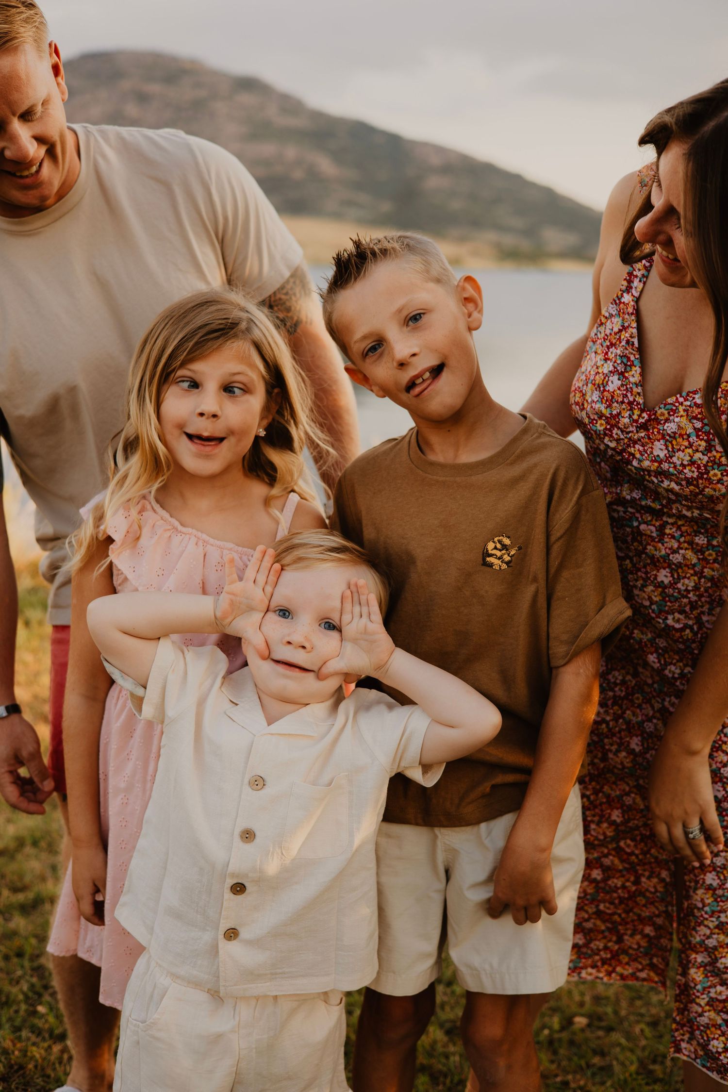 Family group shares candid moments of laughter against mountain landscape at sunset.