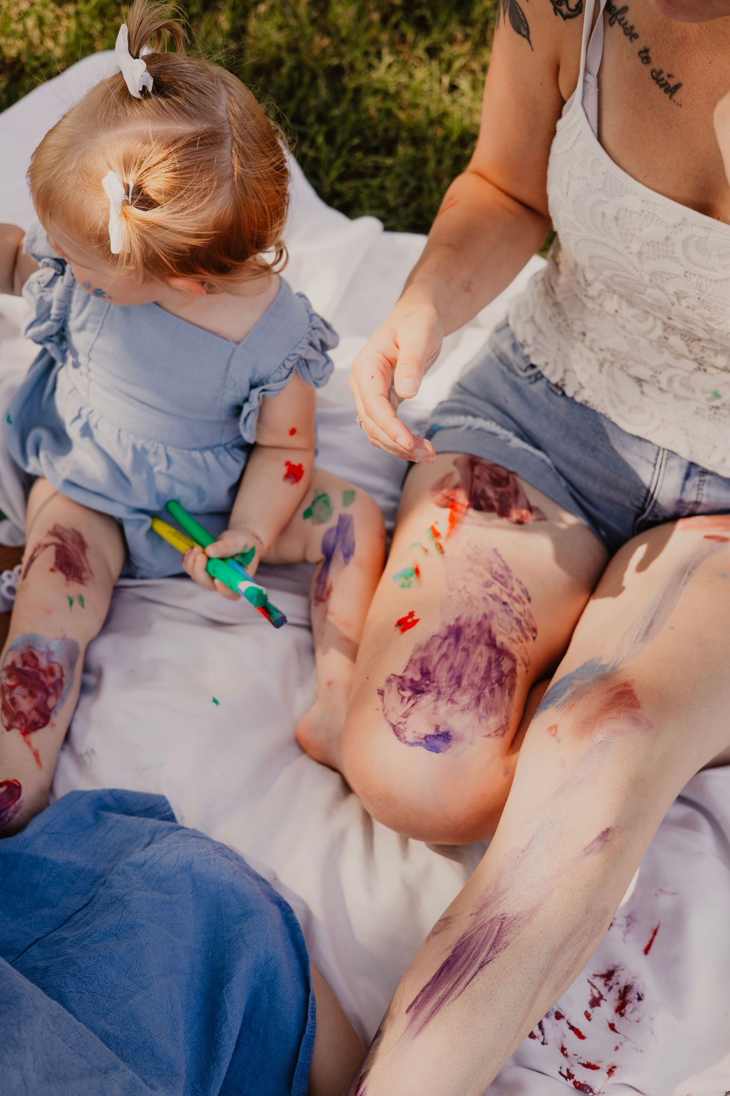 Children sit together painting with colorful paints on a white surface during a creative outdoor art activity.